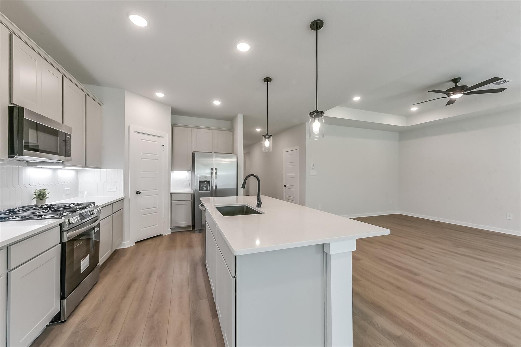 Modern kitchen with white shaker cabinets, stainless appliances, quartz island sink, and open living area in The Everett C, Crosby Texas