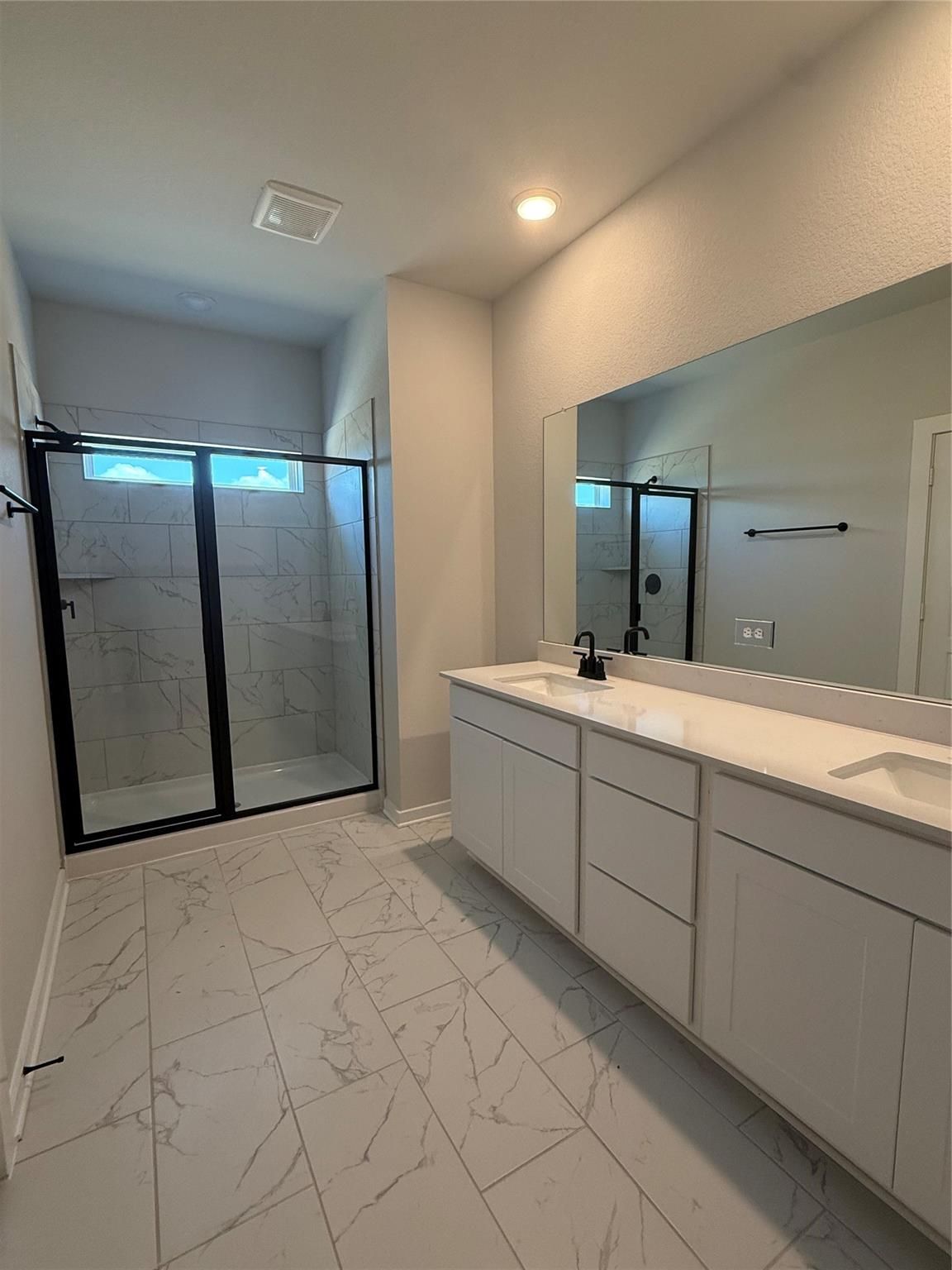 Modern primary bathroom with double vanity, marble-look tile floors, and glass walk-in shower in The Sorrento E, Crosby TX.