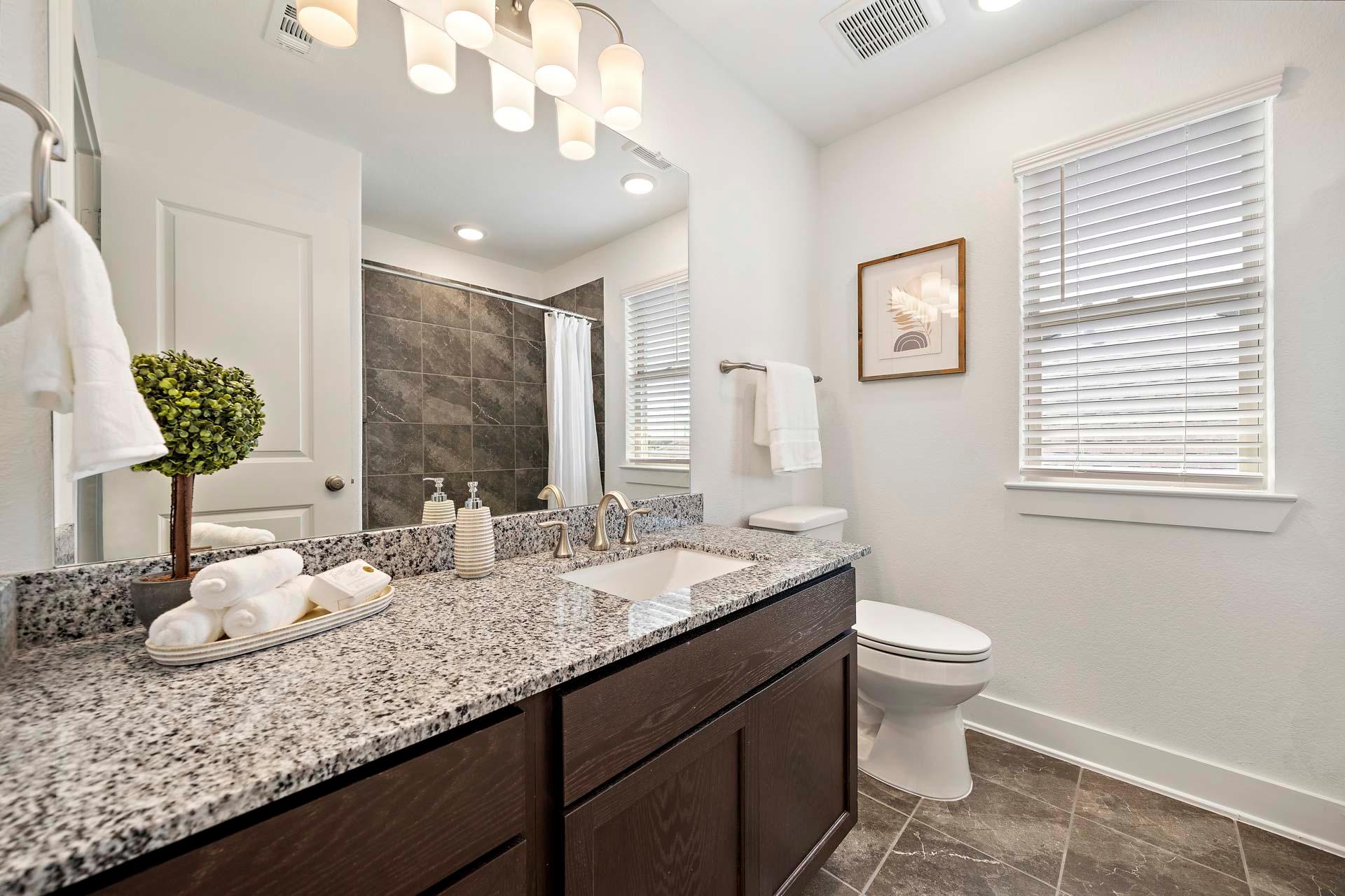 Modern bathroom in Sierra Vista Rosharon Texas with granite double vanity dark cabinets tiled shower and frosted blinds by Davidson Homes