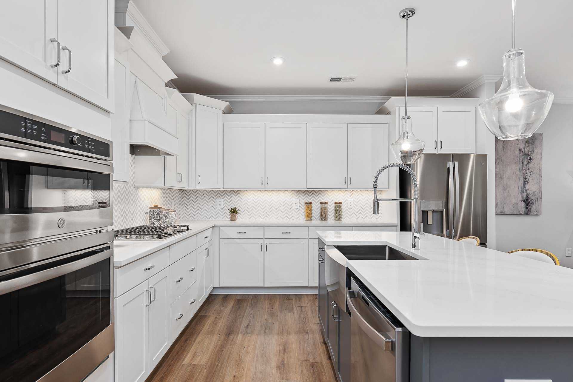 Modern white shaker kitchen in Glenmere, Knightdale NC featuring island with farmhouse sink, stainless appliances, subway backsplash