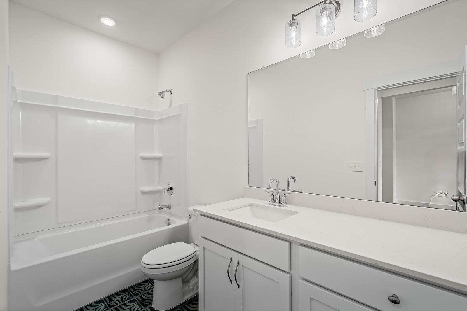 Modern bathroom with white vanity, tub-shower combo, and large mirror in The Ridgeport D at Benders Cove, Mt. Juliet.