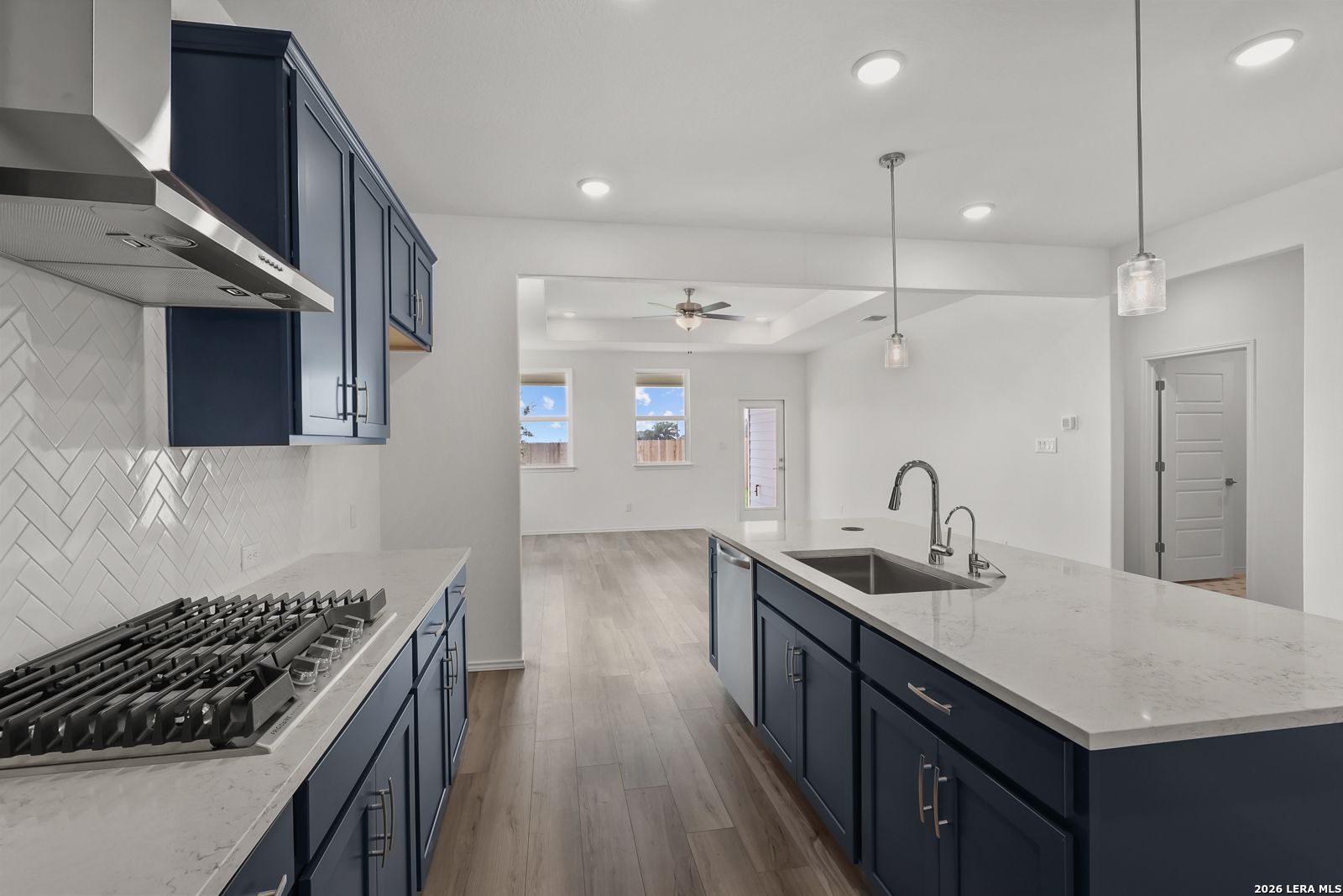 Modern navy kitchen with quartz island, subway tile backsplash, gas range, open to living area in Davidson Homes The Glenwood E, Elmendorf TX