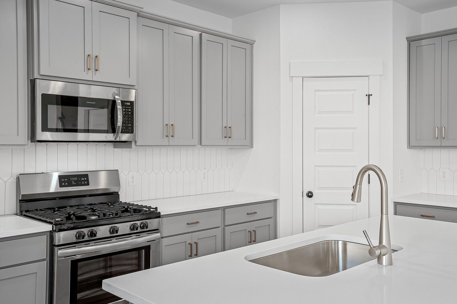 Modern kitchen featuring gray shaker cabinets, stainless steel appliances, and subway tile backsplash in The Logan C by Davidson Homes, Gallatin, TN