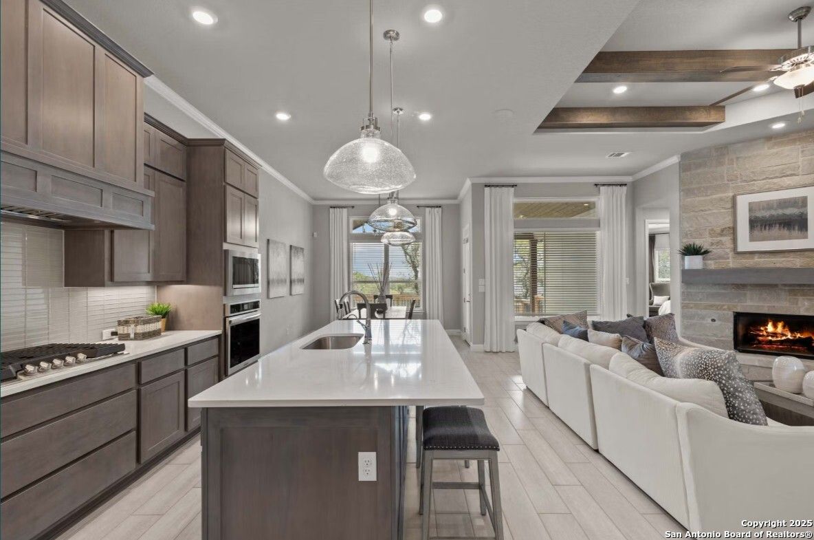 Open-concept kitchen with quartz island, stainless appliances, and adjacent family room featuring stone fireplace and backyard view in The Garner B, Ladera, San Antonio