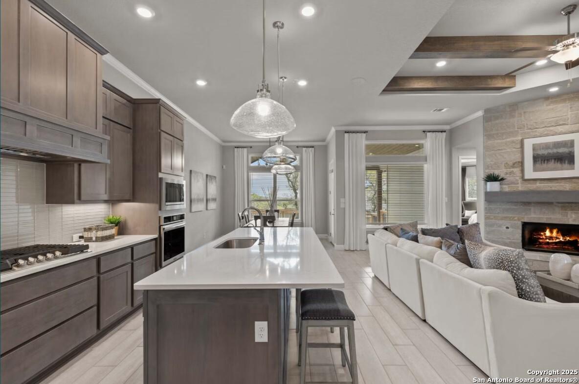 Open-concept kitchen with quartz island, stainless appliances, and adjacent family room featuring stone fireplace and backyard view in The Garner B, Ladera, San Antonio