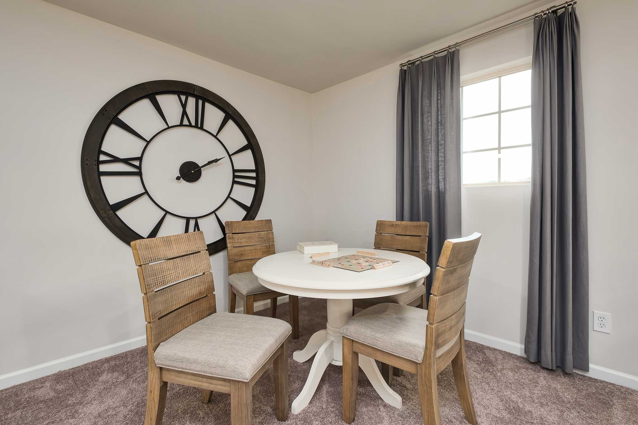 Cozy dining nook at The Reserve at Overton in Hampton Cove, Alabama with round table, wooden chairs, and large wall clock