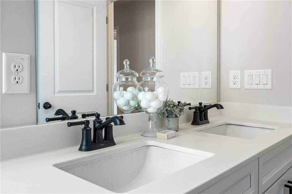 Elegant double vanity with white quartz sinks, black faucets, and decorative jars in master bath of Davidson Homes The Marion C, Winder, GA