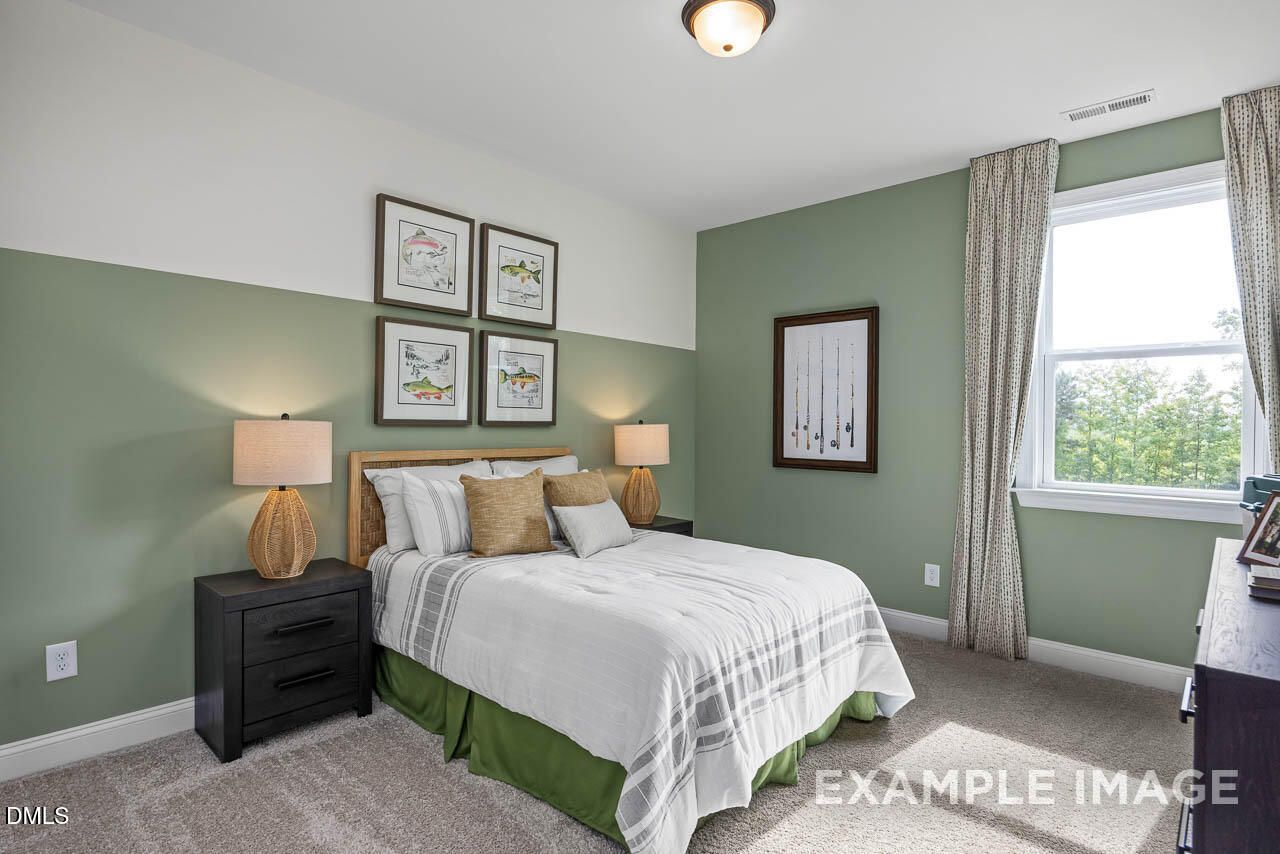 Cozy sage green bedroom with queen bed, woven lamps, framed art, and tree-view window in Davidson Homes Crawford D, Angier, NC
