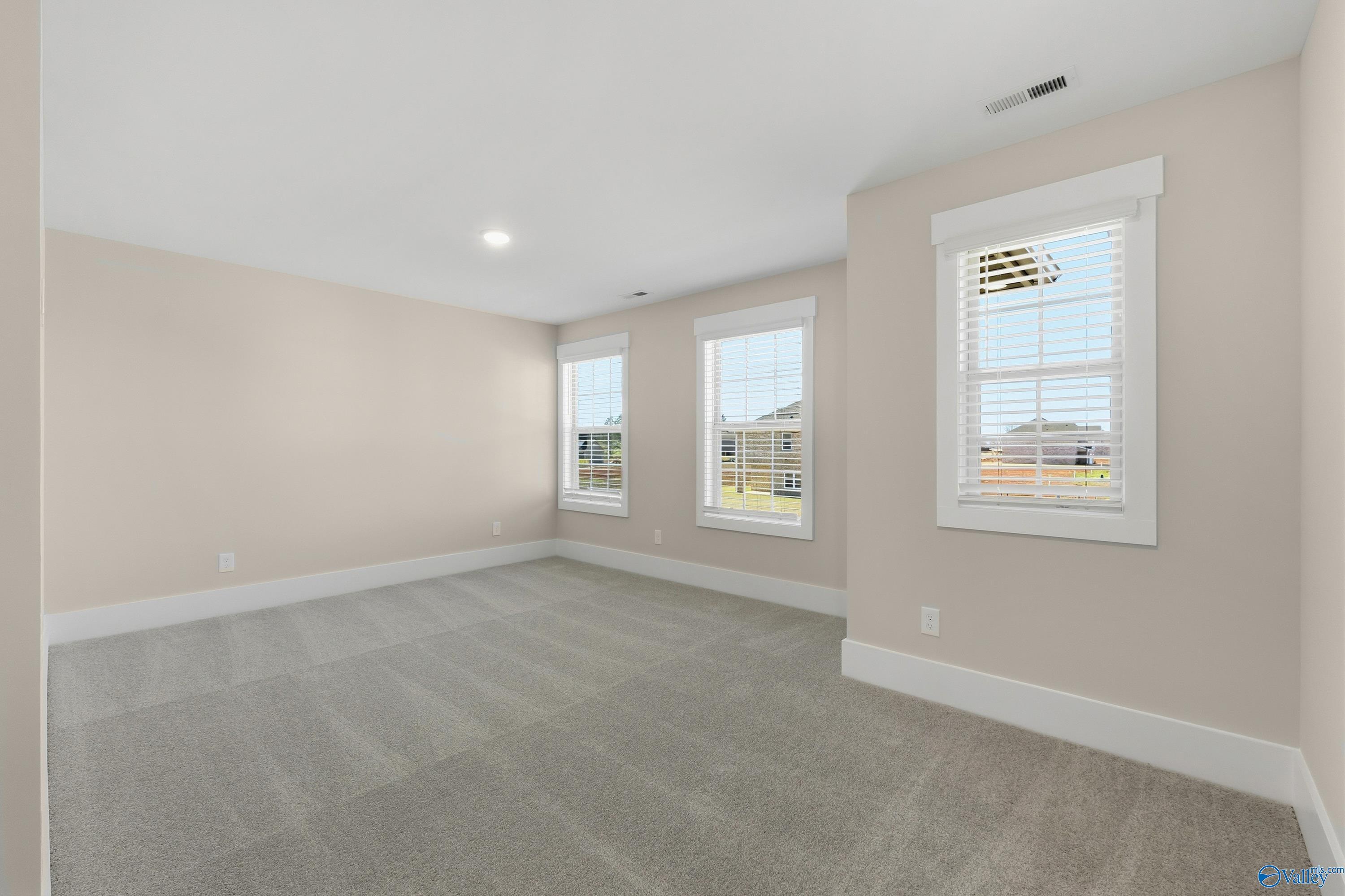 Bright upstairs bedroom with beige walls, gray carpet, and double windows in Davidson Homes The Shelby A, Athens, Alabama