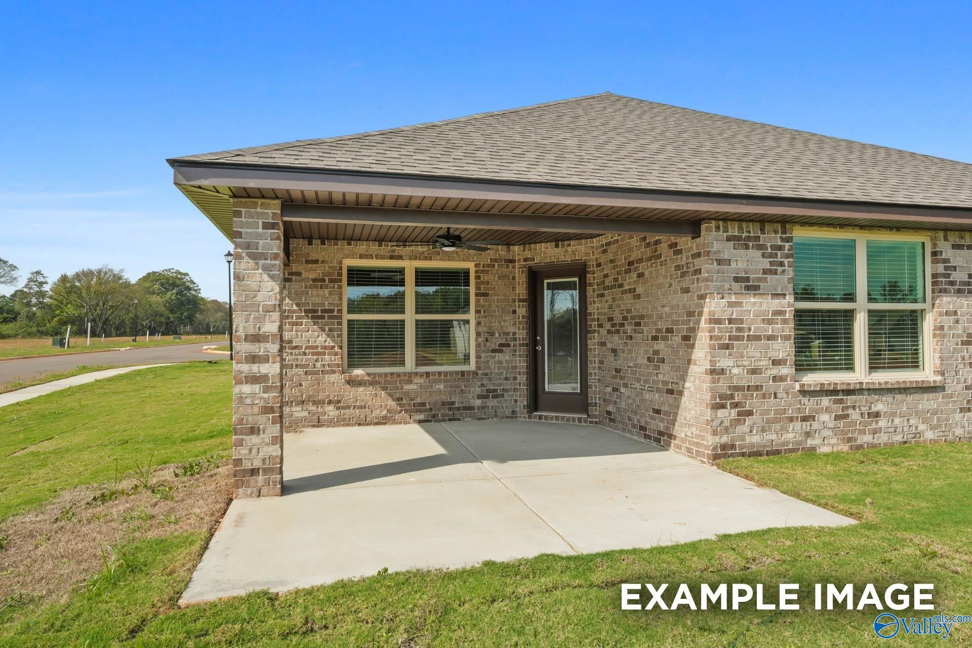 Brick single-story home exterior with covered porch, ceiling fan, brick facade, and lush lawn in Wood Trail, Toney, Alabama by Davidson Homes