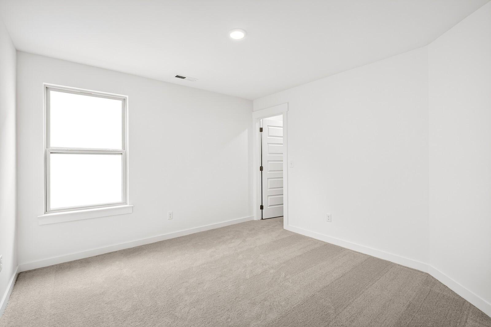 Bright empty bedroom with large window, white walls, and beige carpet in Davidson Homes The Ridgeport C, Gallatin, TN