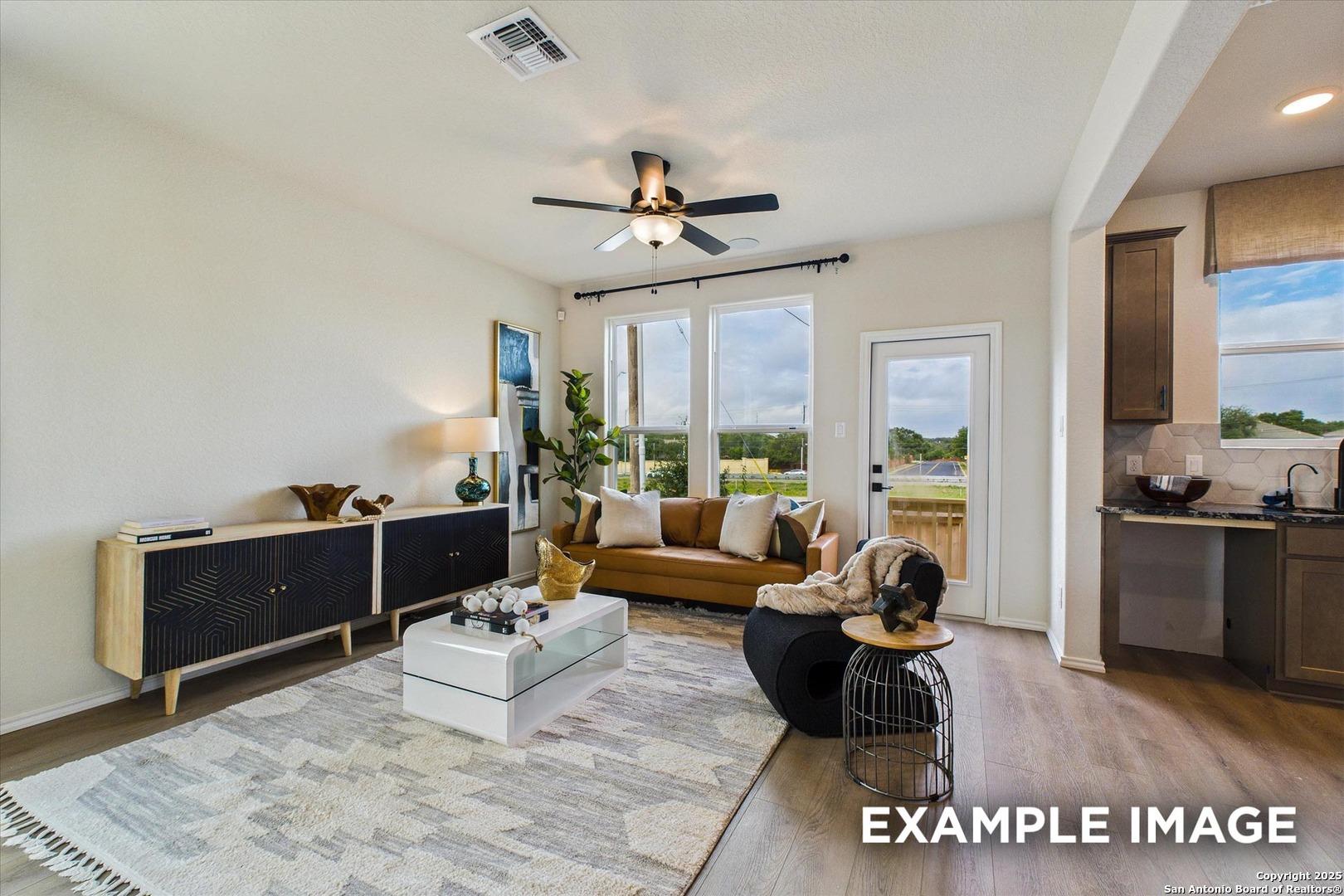 Cozy open living room with beige sofa, ceiling fan, large windows to backyard in Davidson Homes The Florence B, San Antonio