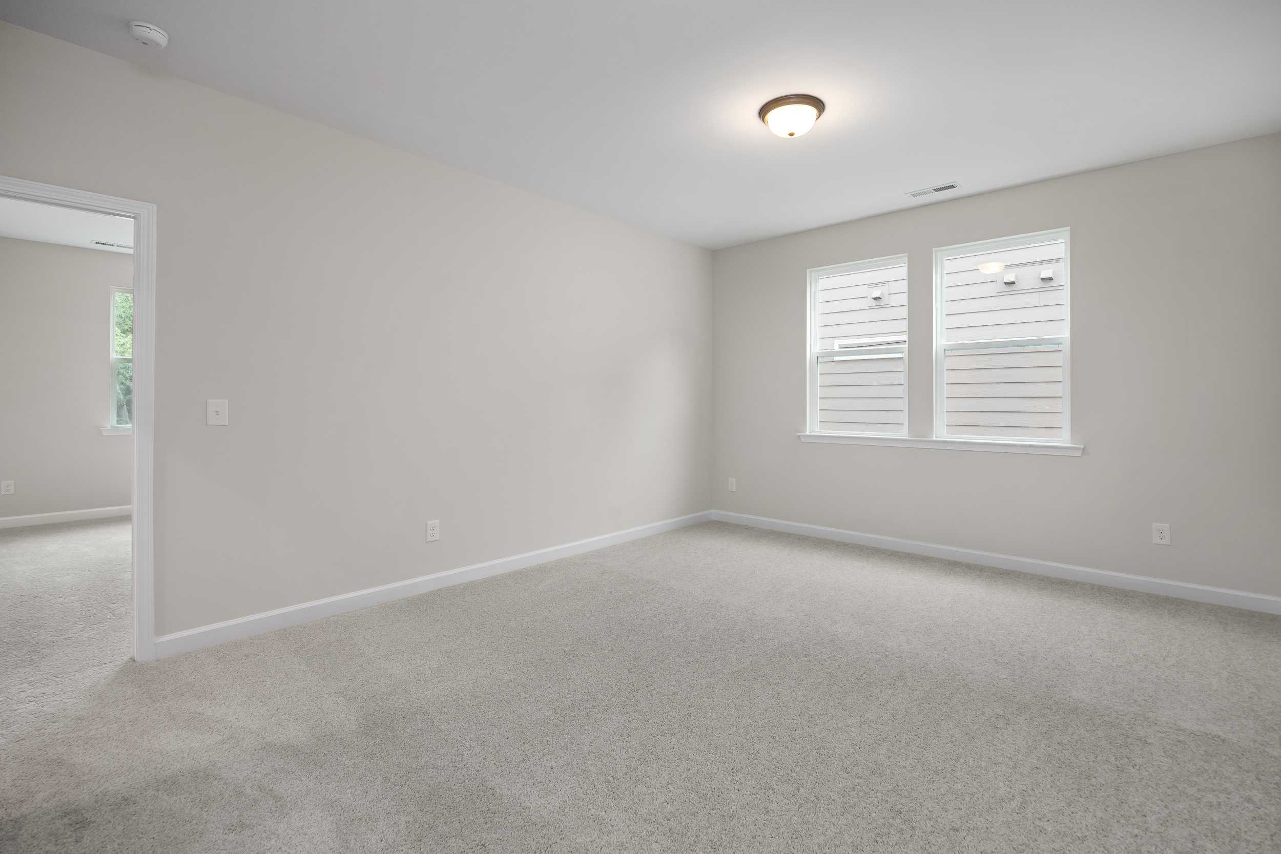 Spacious empty master bedroom in The Beech C featuring neutral beige walls, plush carpet flooring, and double windows with blinds