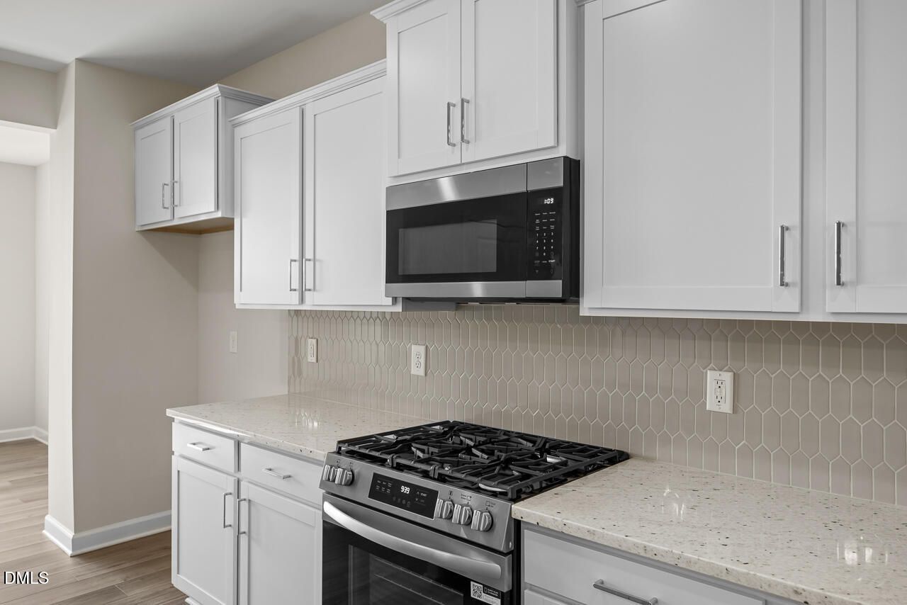 Modern kitchen with white shaker cabinets, gas range, stainless microwave, and hexagon tile backsplash in Davidson Homes Willow C, Zebulon NC