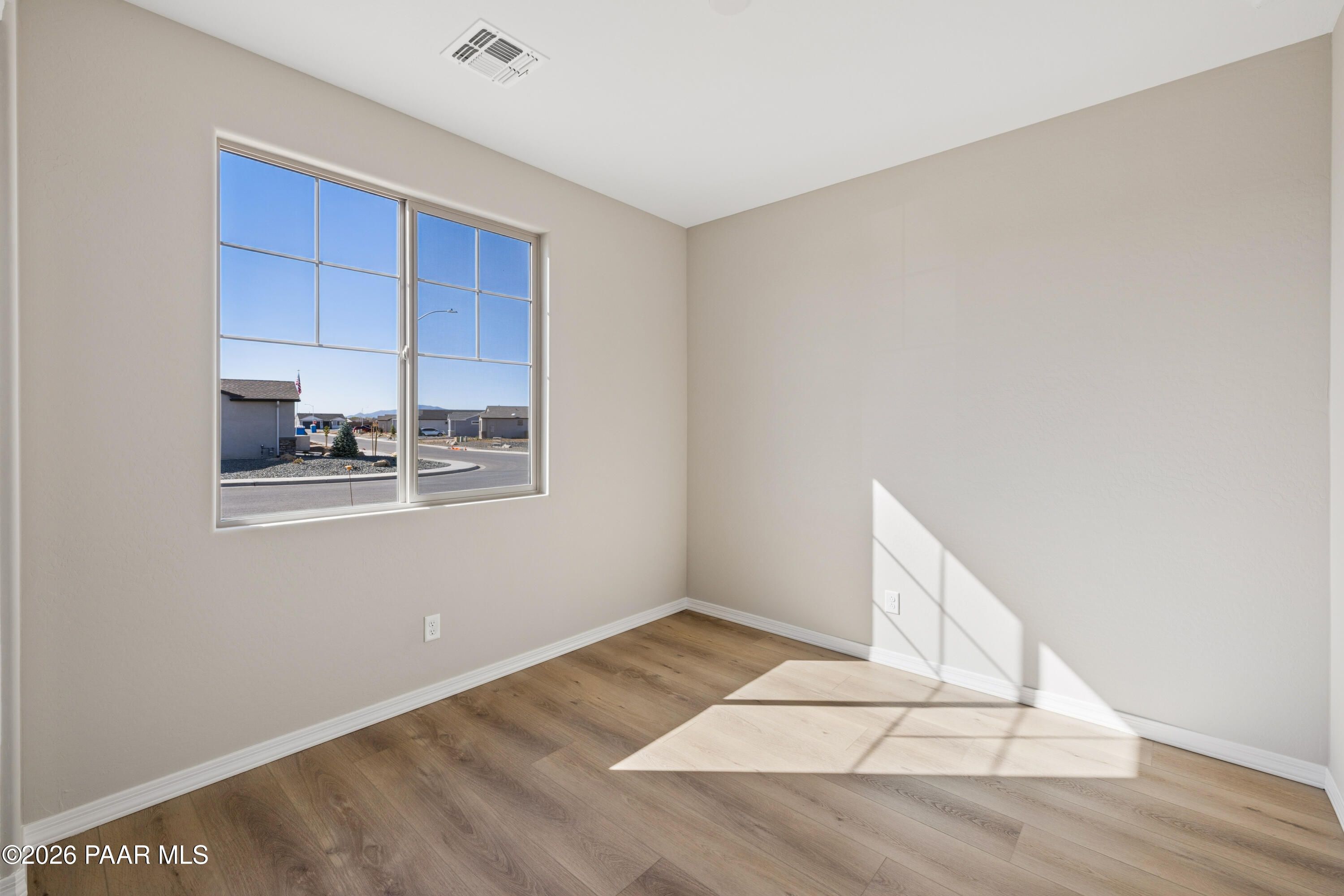 Sunlit secondary bedroom with beige walls, large window overlooking Prescott Valley neighborhood, and wood floors in Davidson Homes The Harmony A