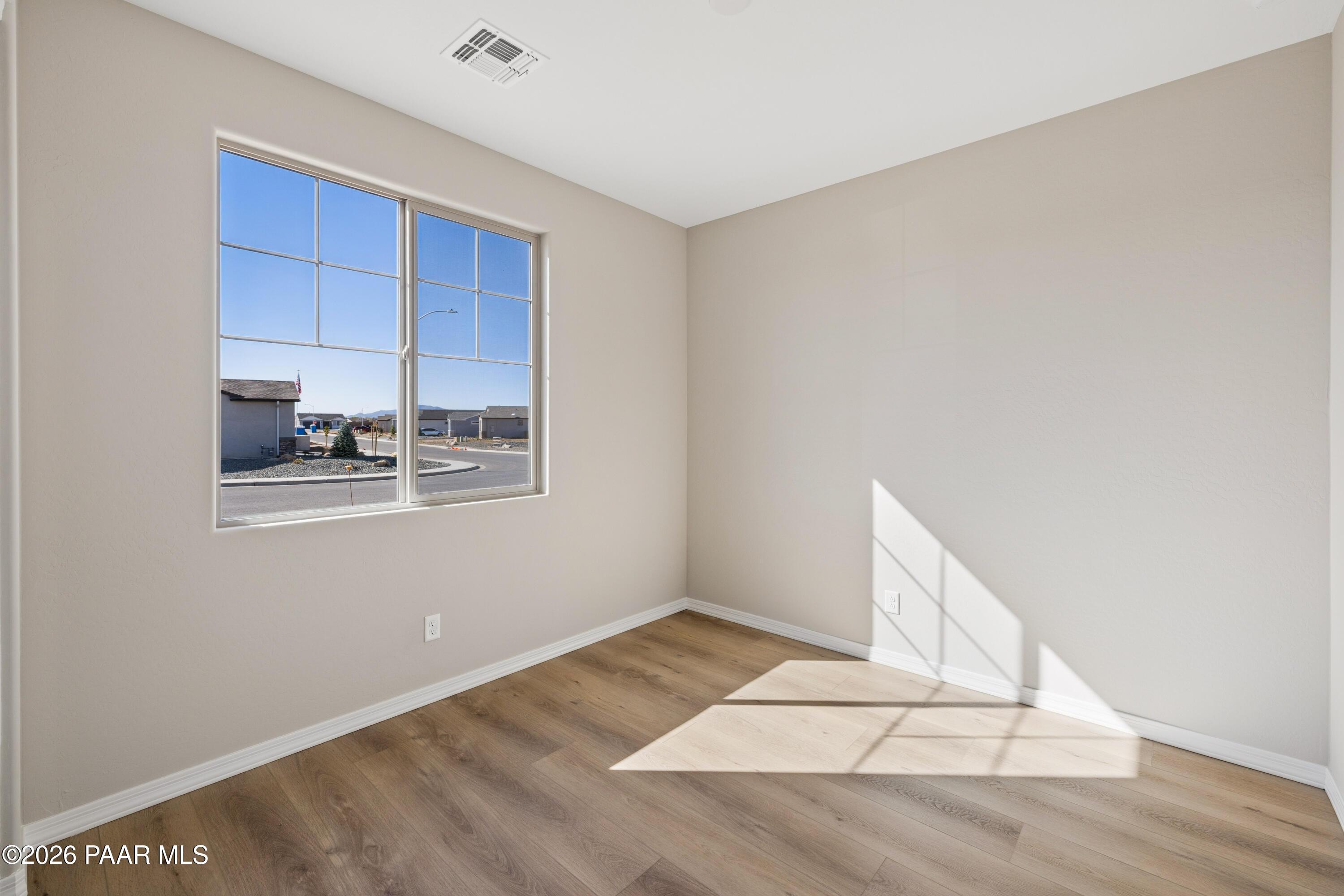 Sunlit secondary bedroom with beige walls, large window overlooking Prescott Valley neighborhood, and wood floors in Davidson Homes The Harmony A