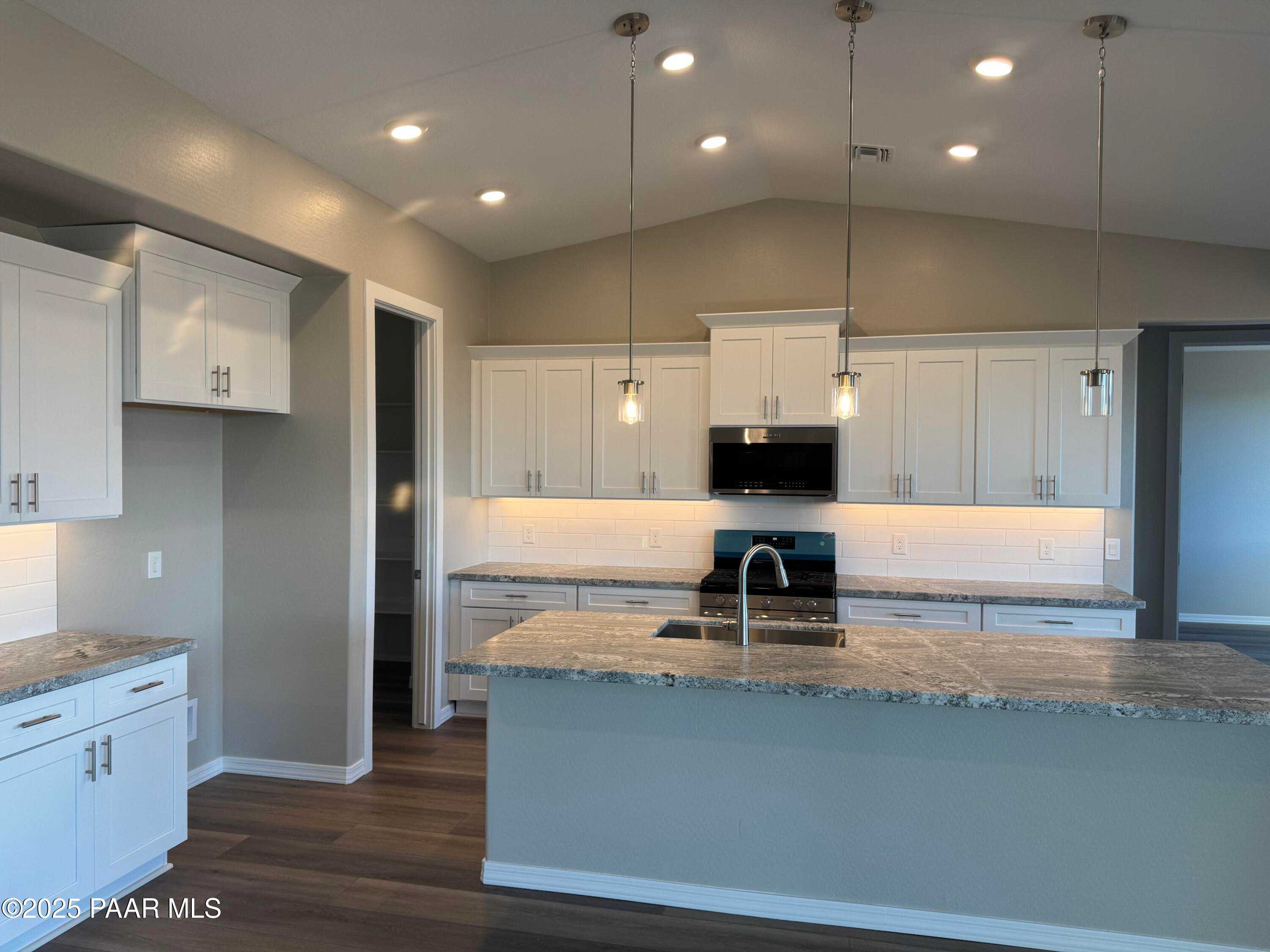 Modern kitchen with white cabinets, granite island, stainless microwave and cooktop in Davidson Homes The Monarch A, Prescott AZ