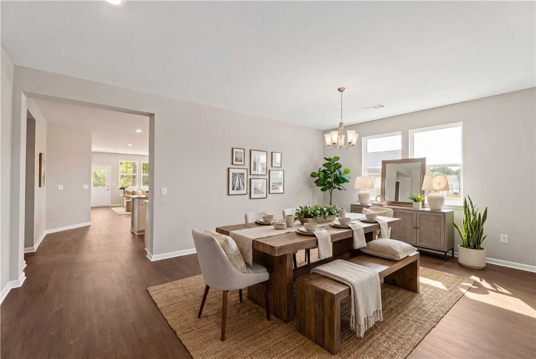Elegant dining room with wooden farmhouse table, upholstered chairs, potted plants, and gallery wall in Evermore Homes The Orion, Cusseta, Alabama