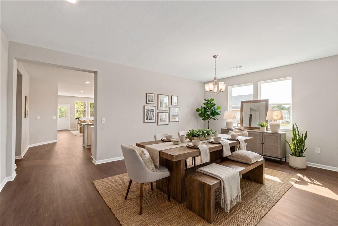 Elegant dining room with wooden table, beige chairs, potted plants, and artwork in open layout, The Orion by Evermore Homes, Cusseta, Alabama