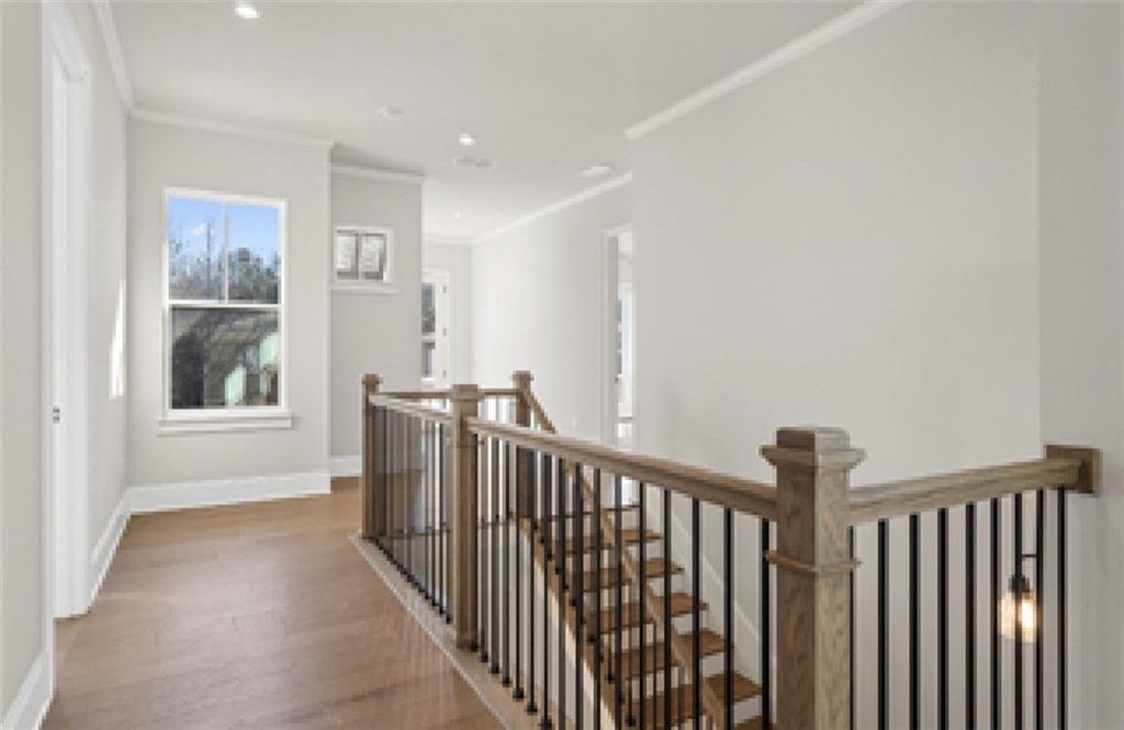 Elegant wooden staircase with wrought iron balusters and upstairs hallway in Davidson Homes The Seaside A, Woodstock, GA