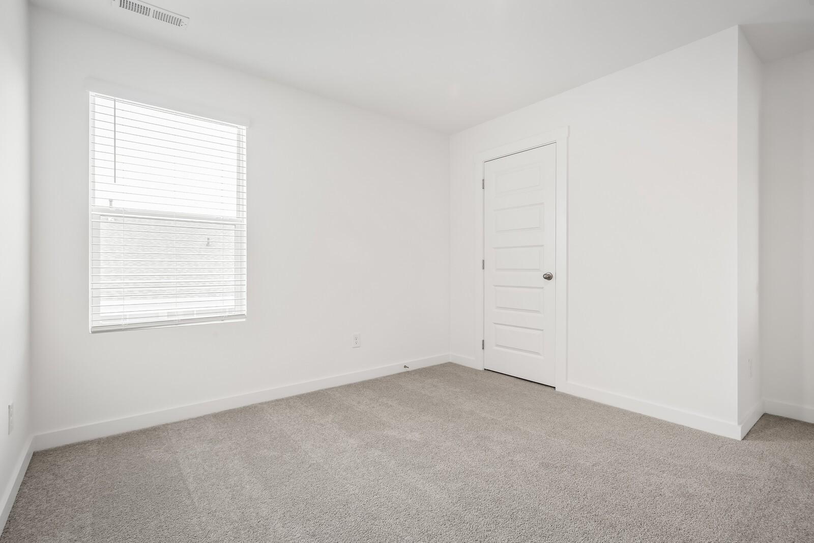 Bright secondary bedroom with white walls, window blinds, white door, and beige carpet in Davidson Homes The Gordon C, White House, TN