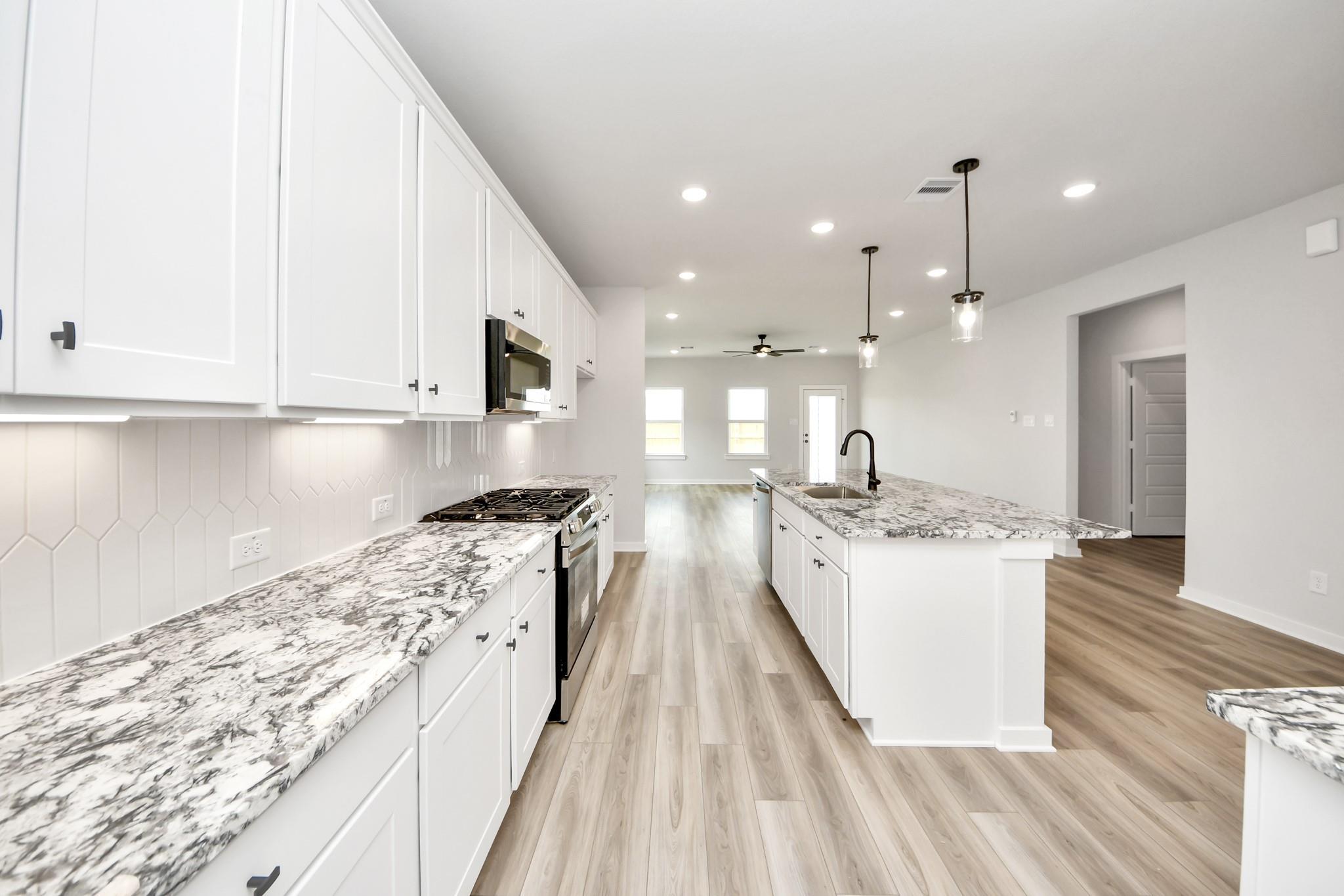 Modern kitchen with white cabinets, granite island, and wood flooring in The Sorrento E floor plan, Sundance Cove, Crosby.