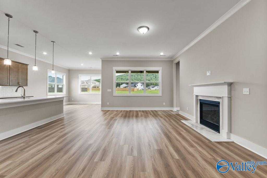 Open-concept living room with hardwood floors, white fireplace, kitchen island, and large windows in Evermore Homes The Oxford, Owens Cross Roads, AL