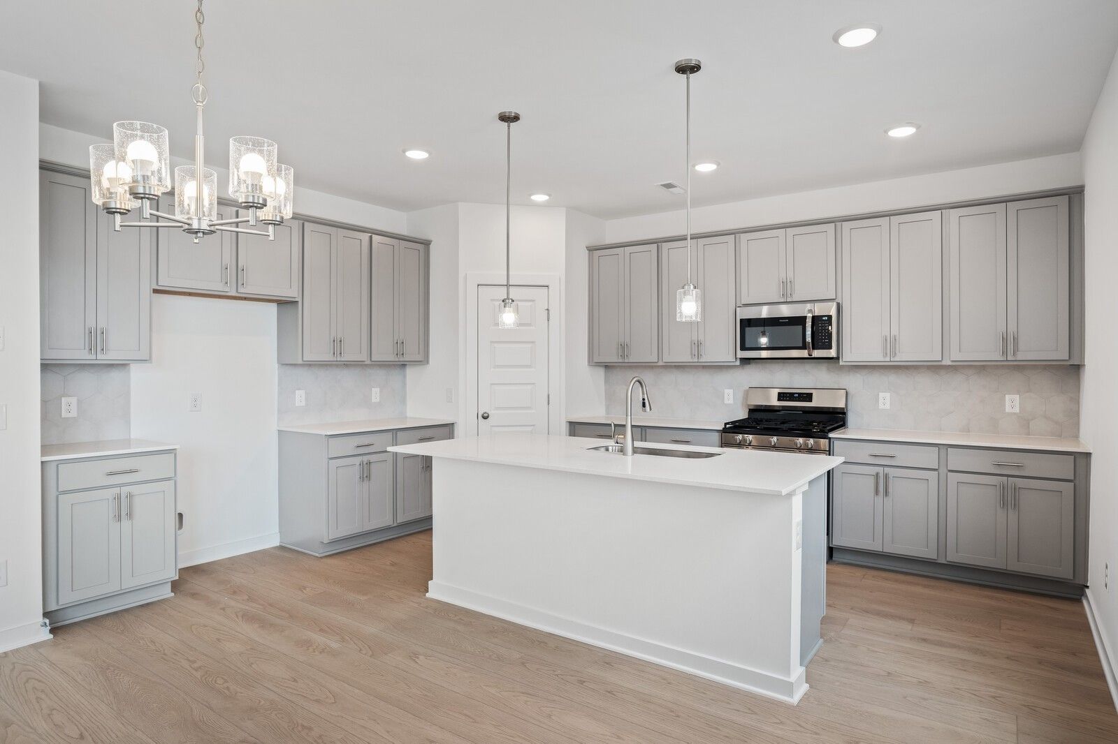 Modern kitchen with gray cabinets, quartz island, and stainless steel appliances in The Logan C floor plan, White House, TN.