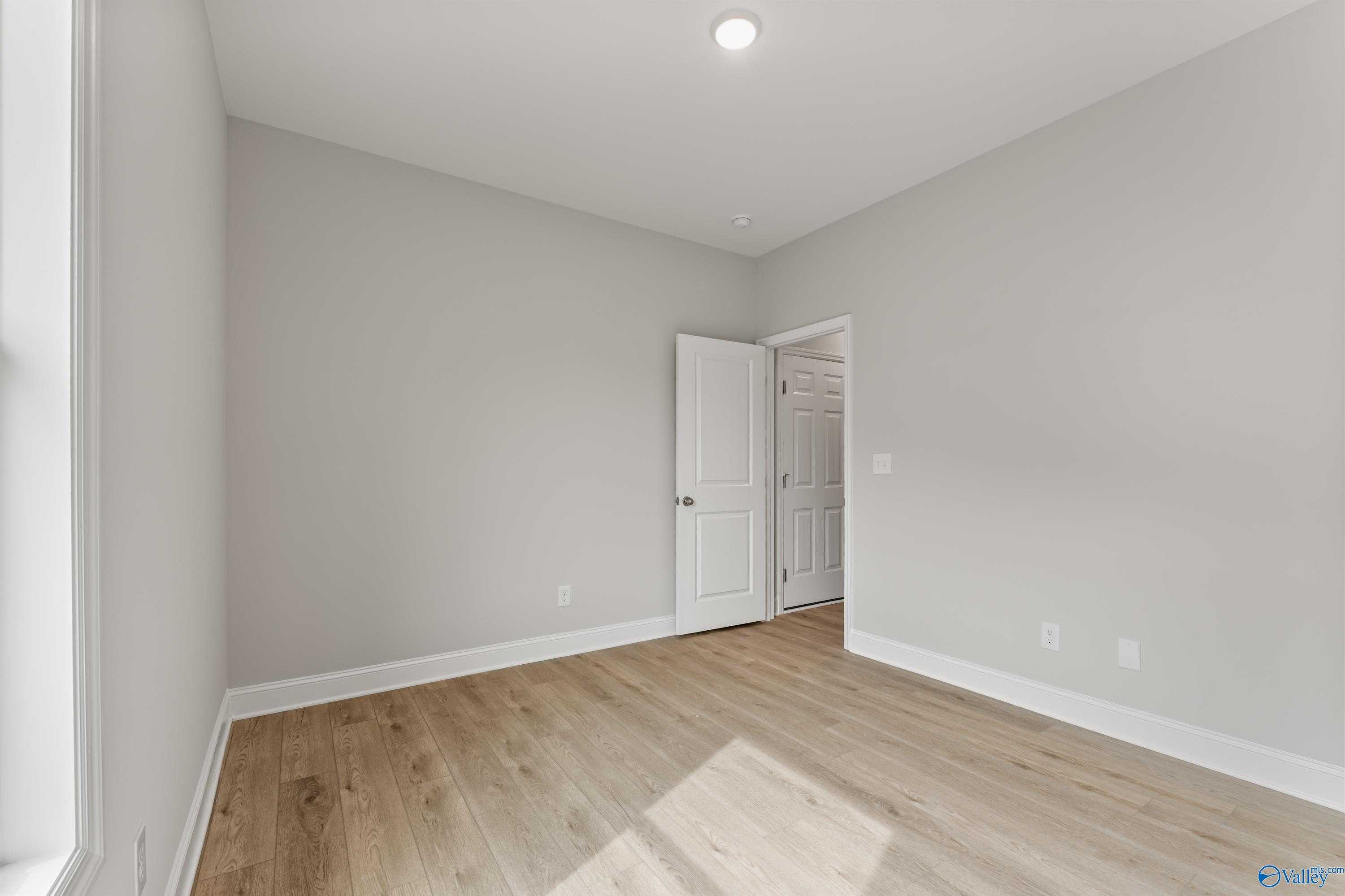 Empty bedroom featuring light gray walls, white door, and hardwood floors in Davidson Homes The Daphne C, Athens, Alabama