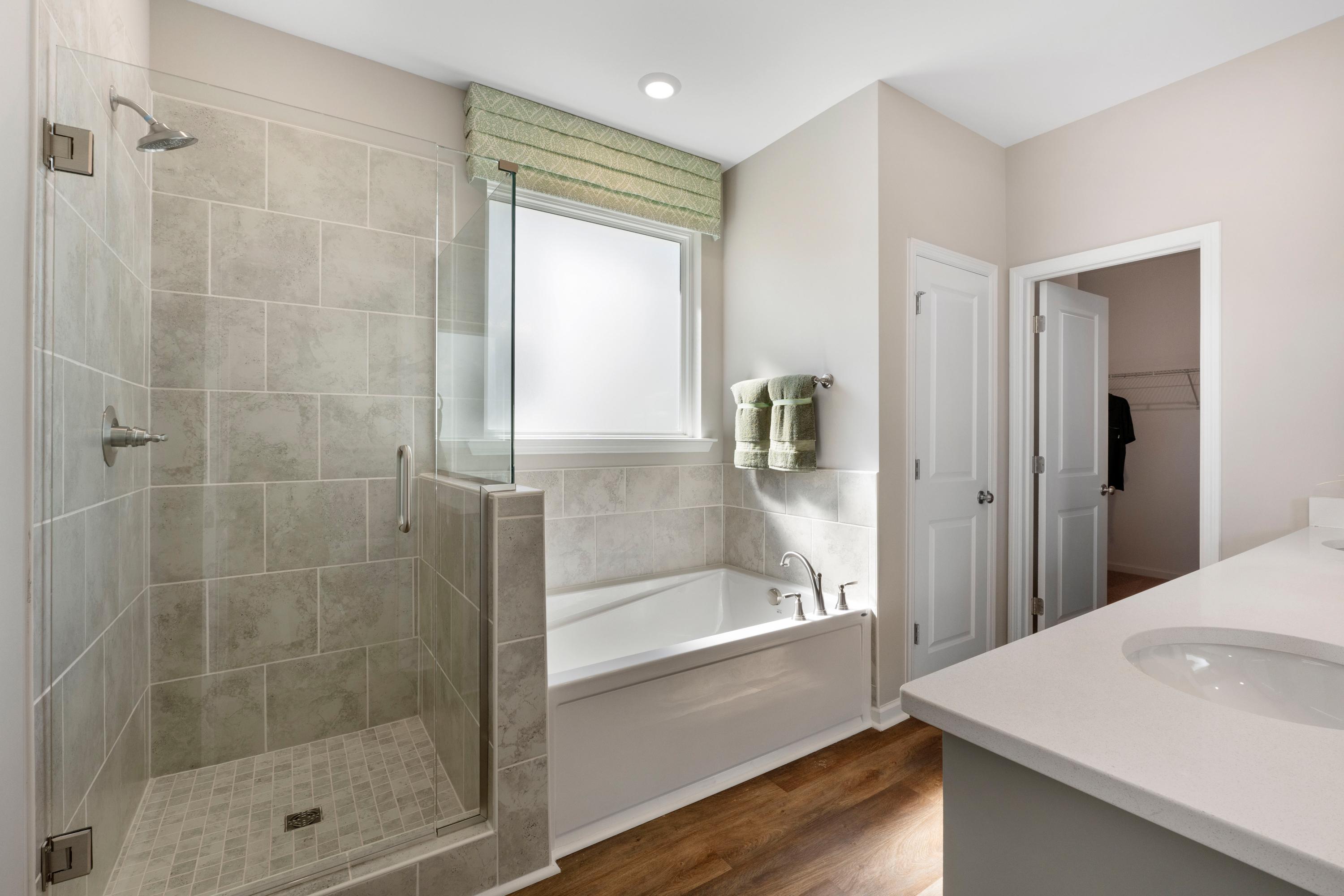 Luxurious primary bathroom in Evergreen Mill, Madison Alabama with tiled walk-in shower, soaking tub and wood floors