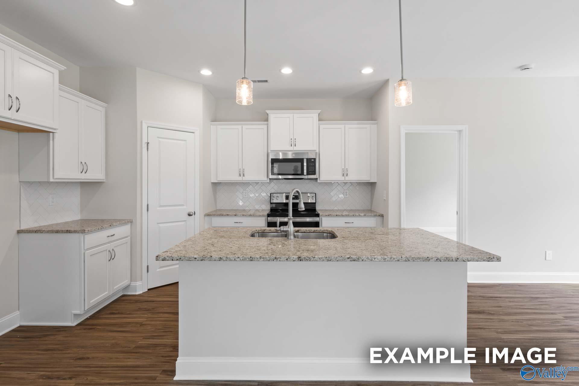 Modern white kitchen with granite island, stainless appliances, pendant lights in The Franklin 3-bedroom home, Meridianville, AL