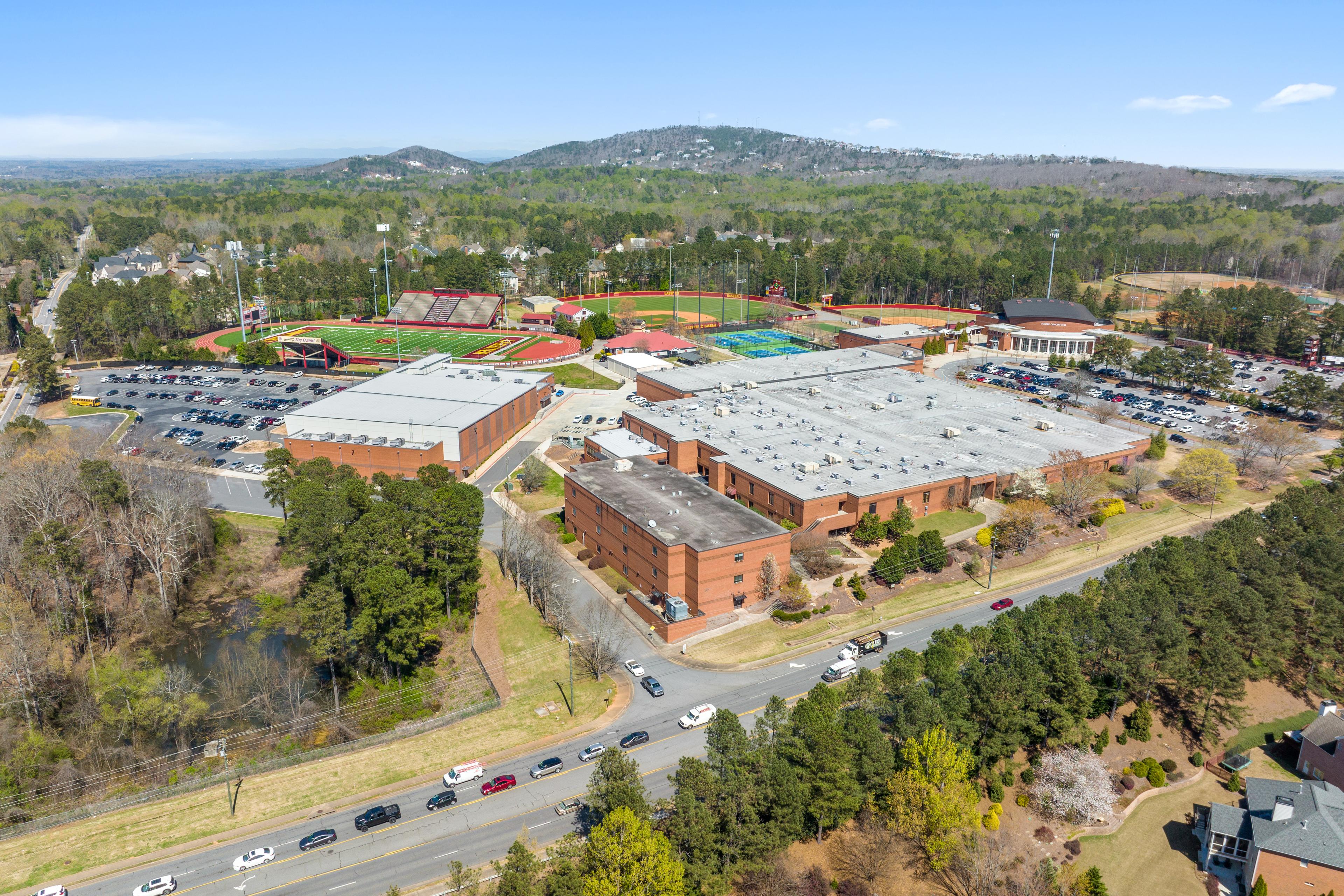 Aerial view of Lassiter High School campus in East Cobb Georgia featuring red track field, brick buildings, parking lots and pine woodlands