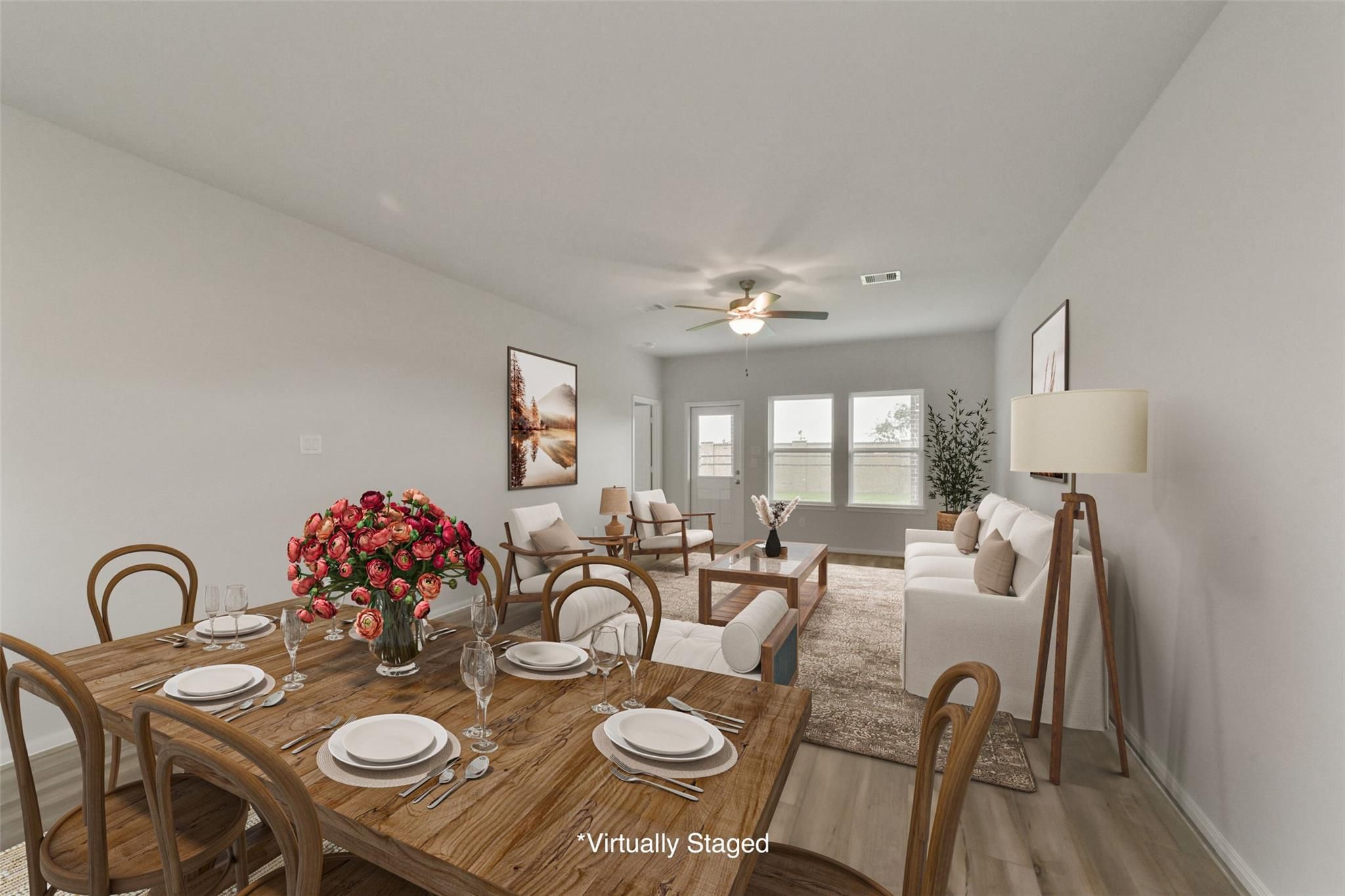 Open dining-living area with wooden table, red floral centerpiece, white sofa, and large windows in The San Marcos E by Davidson Homes, Beasley, Texas