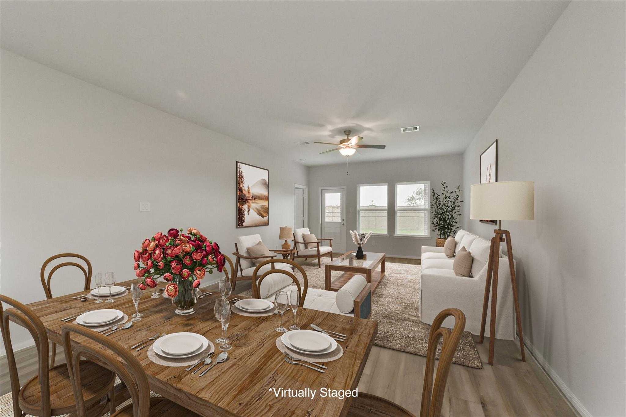 Open dining-living area with wooden table, red floral centerpiece, white sofa, and large windows in The San Marcos E by Davidson Homes, Beasley, Texas