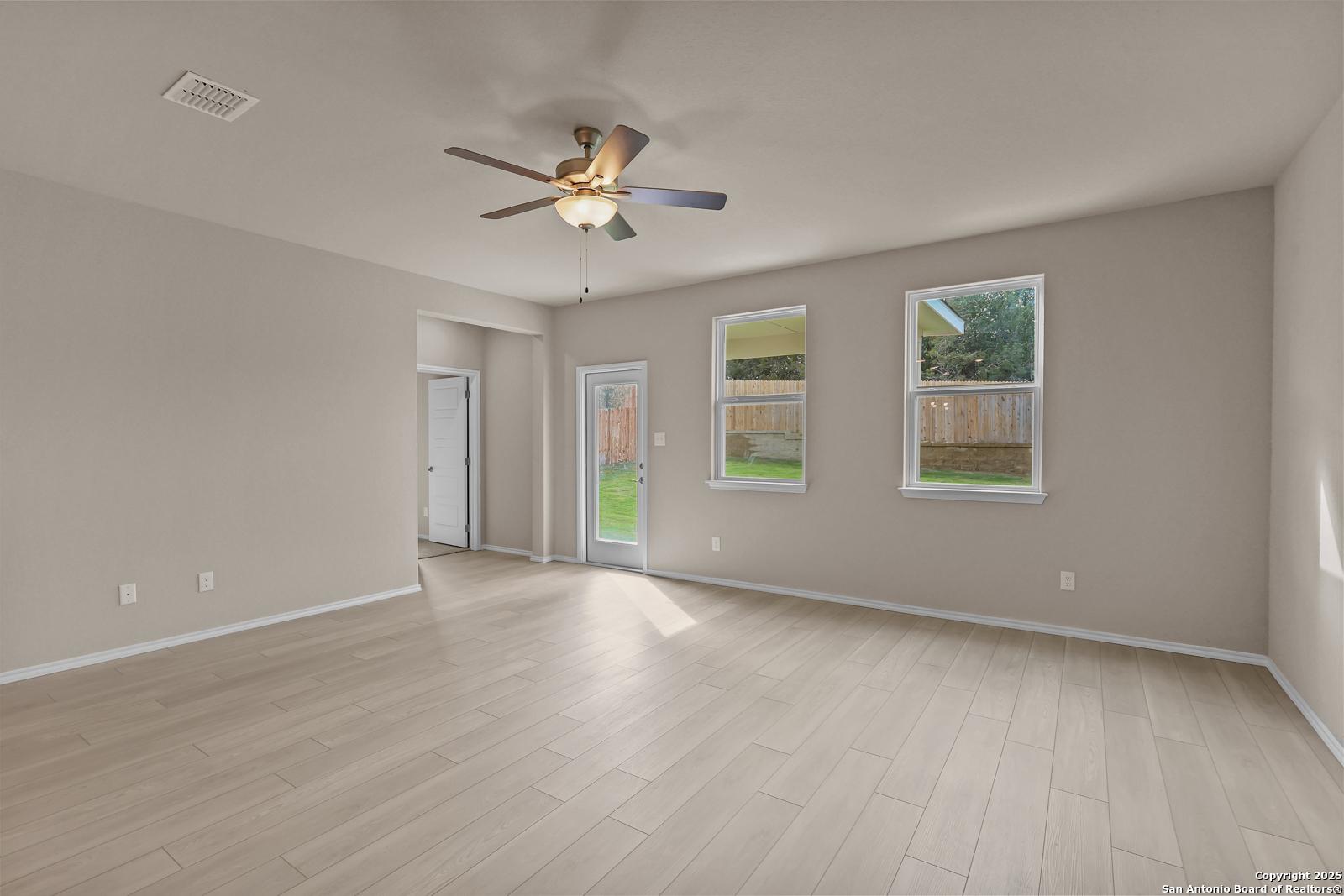 Bright family room with light wood floors, gray walls, ceiling fan, large windows, and sliding door to fenced backyard in Davidson Homes The Douglas G, San Antonio