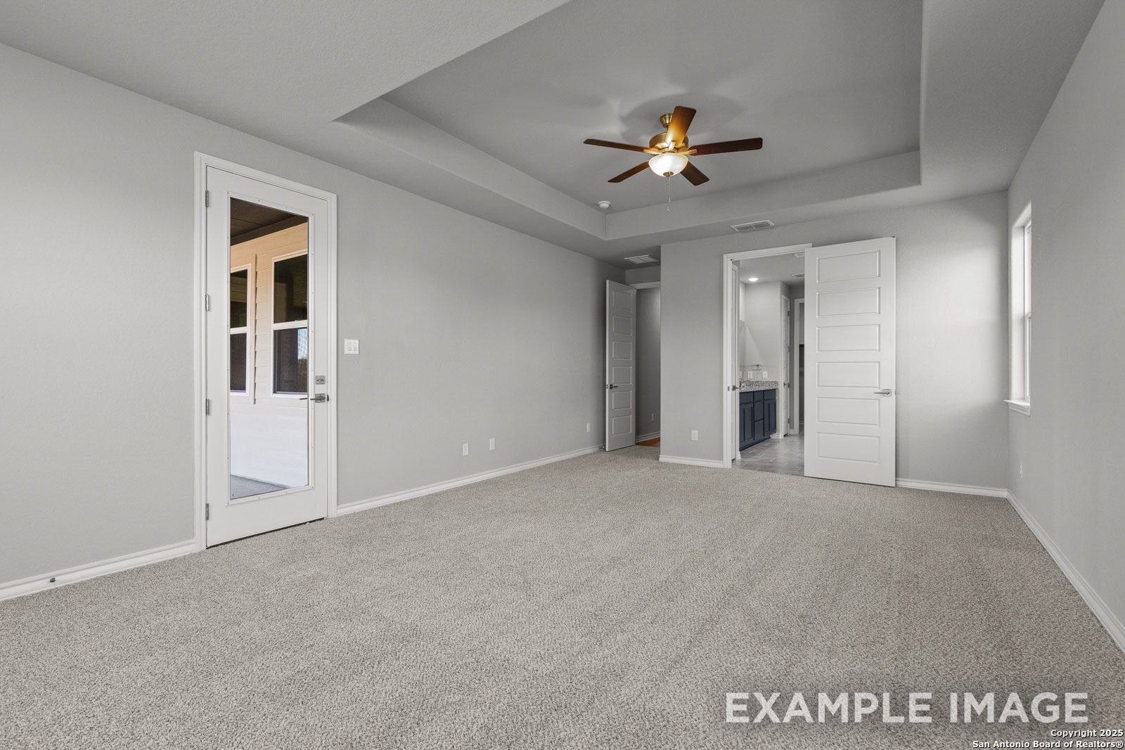 Spacious master suite in The Oxford H featuring a tray ceiling, ceiling fan, and direct access to a private bathroom.