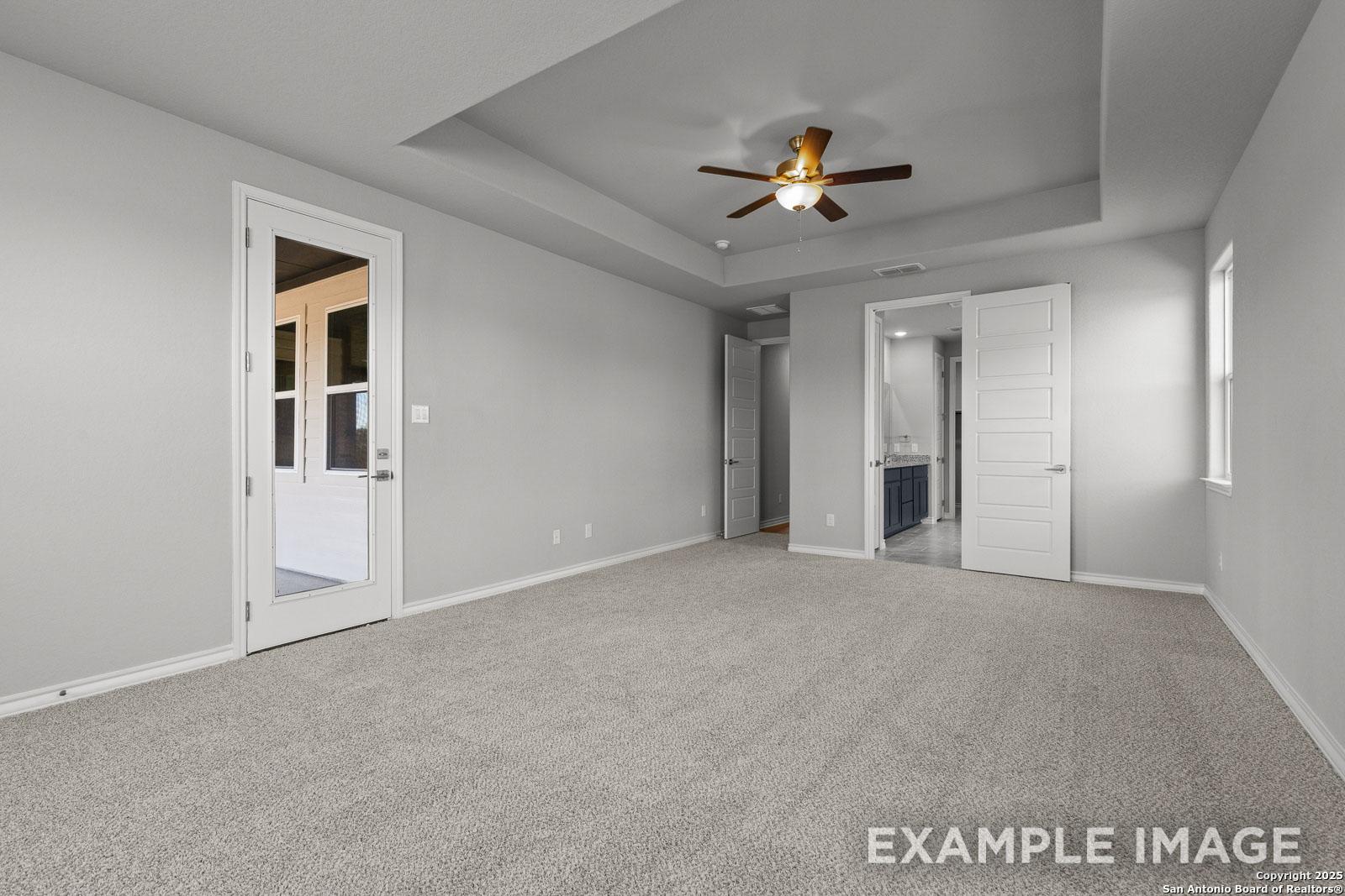 Spacious master suite in The Oxford H featuring a tray ceiling, ceiling fan, and direct access to a private bathroom.