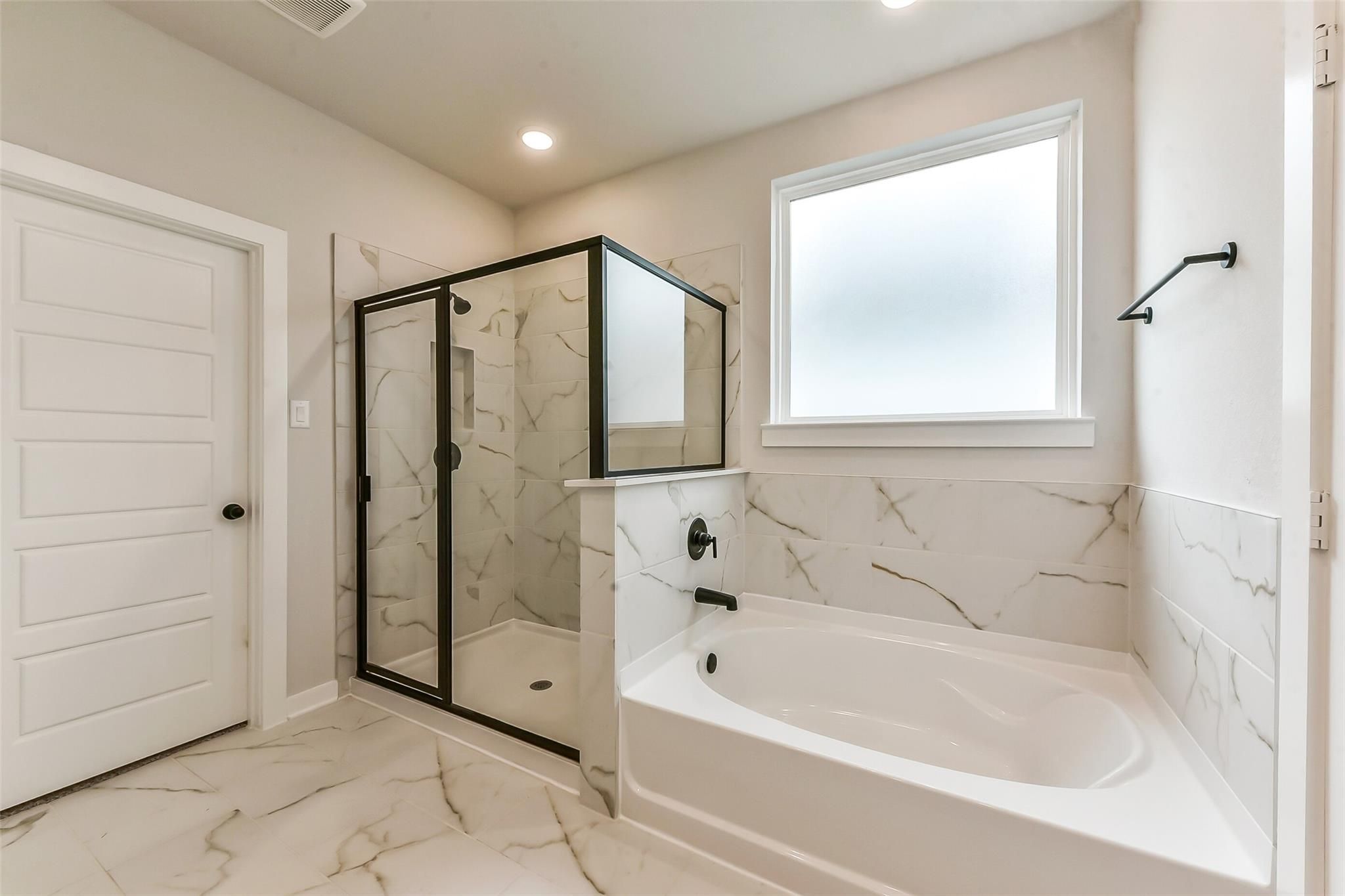 Modern master bath with black-framed glass shower, white soaking tub, marble tiles in Davidson Homes Sequoia C, Crosby TX