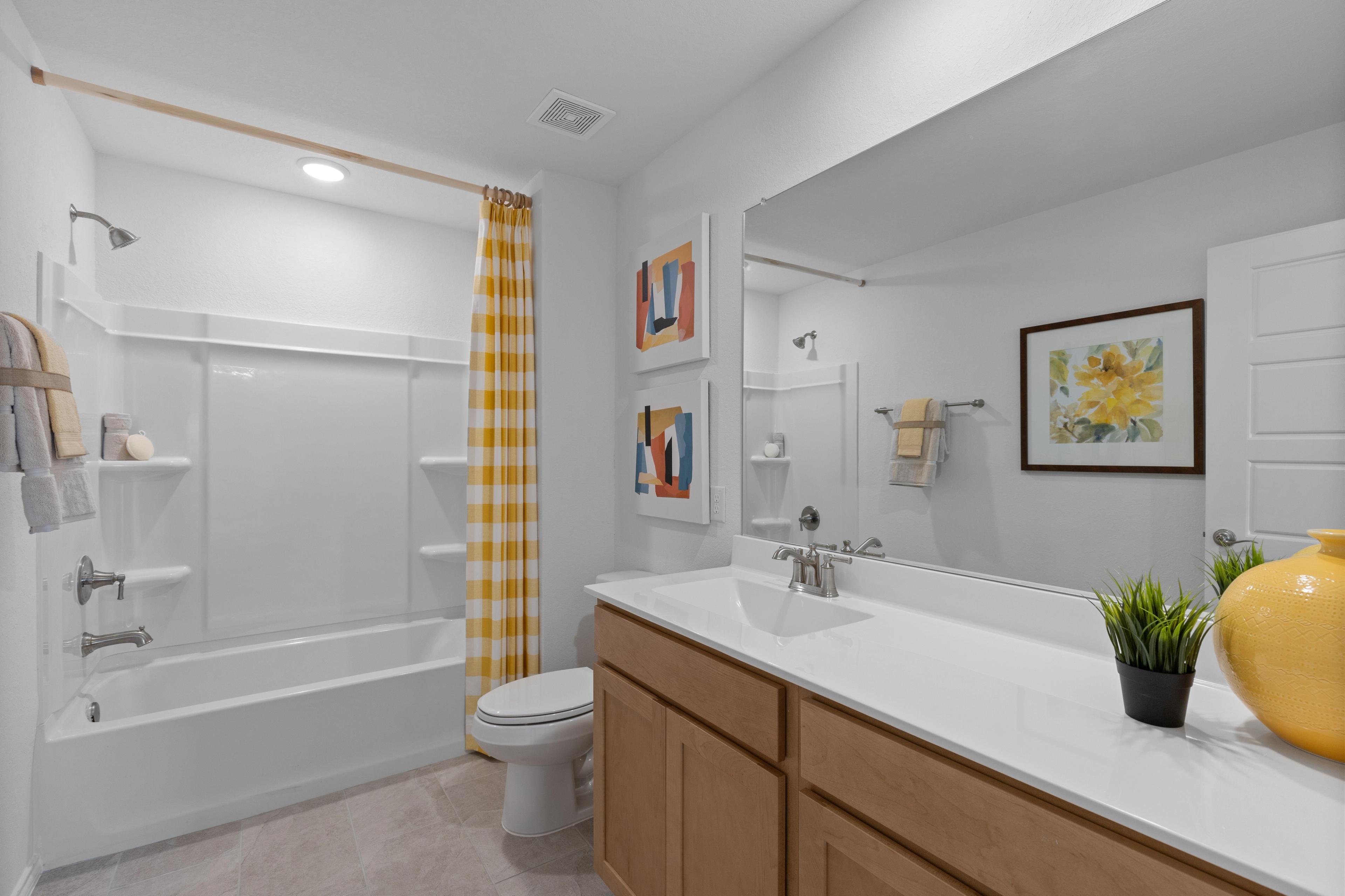 Modern bathroom at Horizon Pointe in Converse Texas featuring yellow gingham shower curtain bathtub and oak vanity