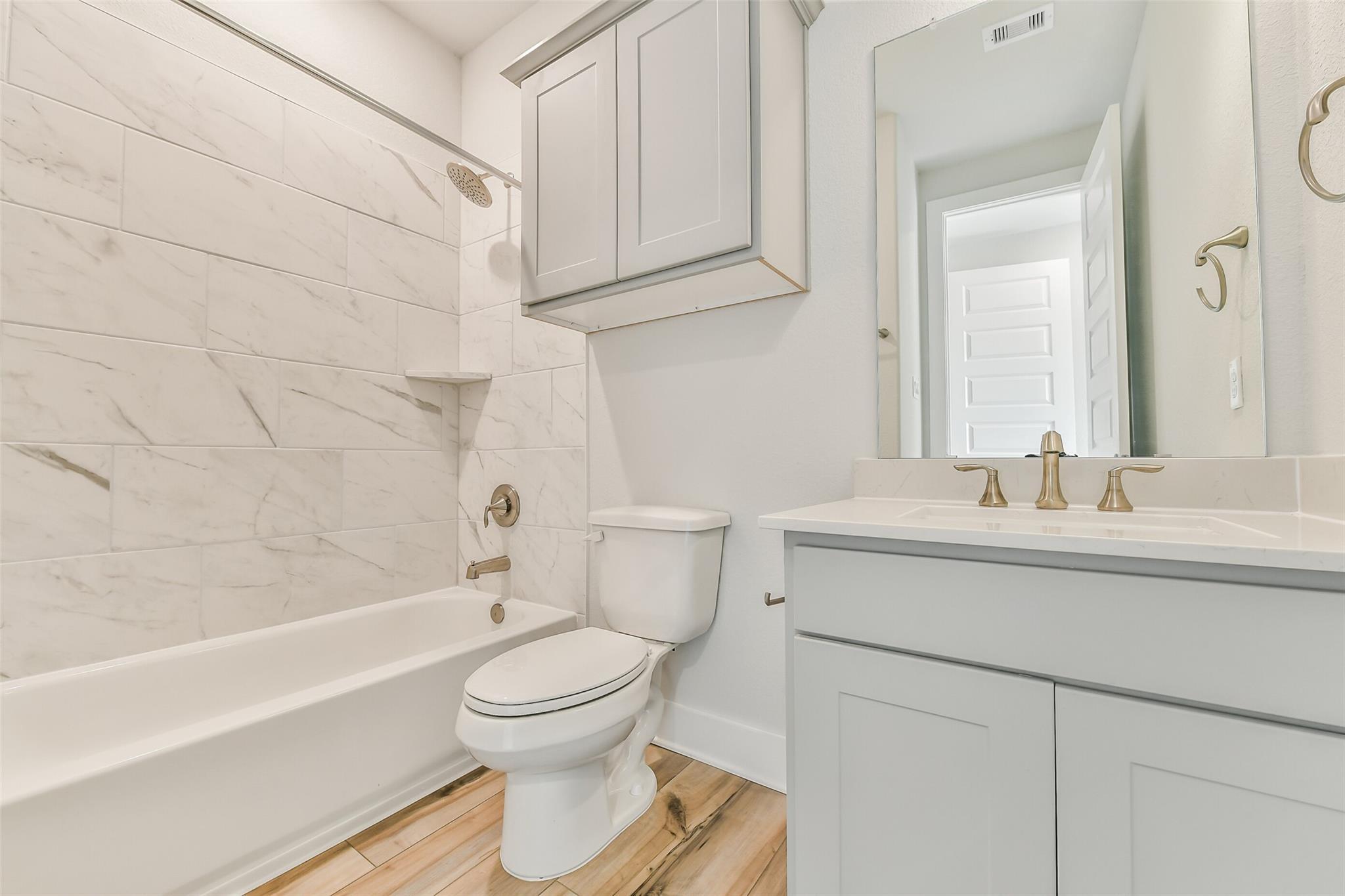 Modern guest bathroom with white subway tile shower, soaking tub, double vanity, and hardwood floors in Davidson Homes The George A, Lago Mar, Texas City