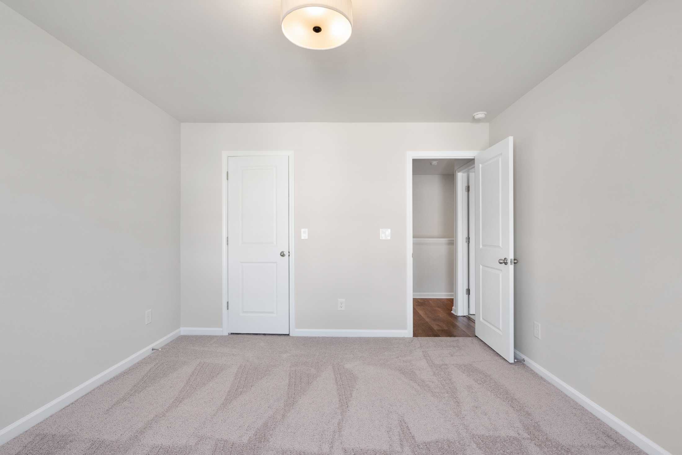 Spacious empty bedroom in The Cary B home design with beige walls, carpet flooring, double doors, and ceiling light fixture