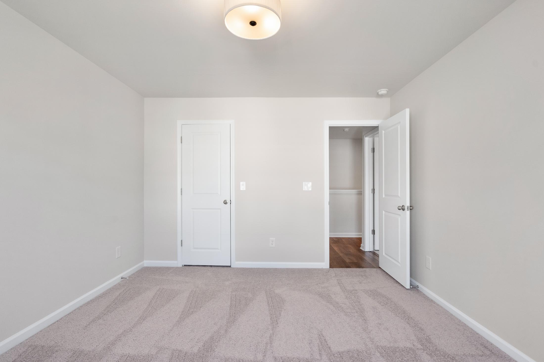 Spacious empty bedroom in The Cary B home design with beige walls, carpet flooring, double doors, and ceiling light fixture
