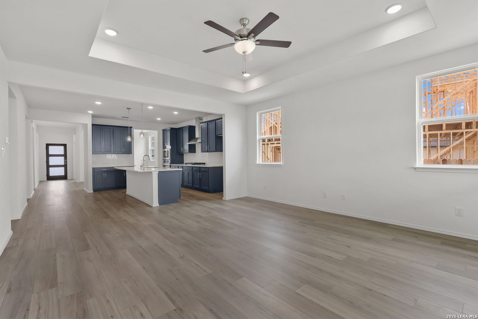 Open-concept living and kitchen with navy cabinets, white island, ceiling fan, and wood floors in Davidson Homes The Glenwood E, Elmendorf, Texas