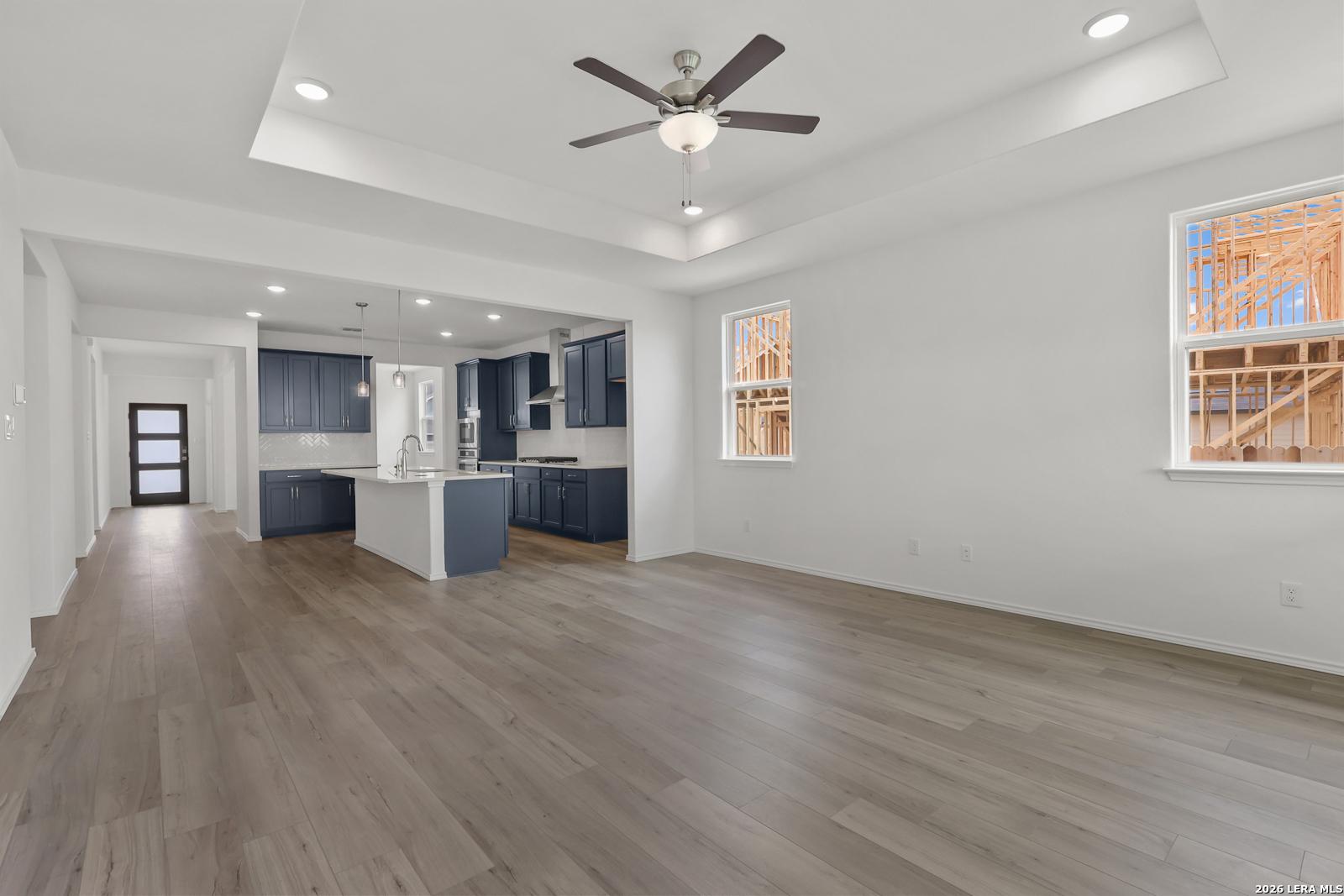 Open-concept living and kitchen with navy cabinets, white island, ceiling fan, and wood floors in Davidson Homes The Glenwood E, Elmendorf, Texas