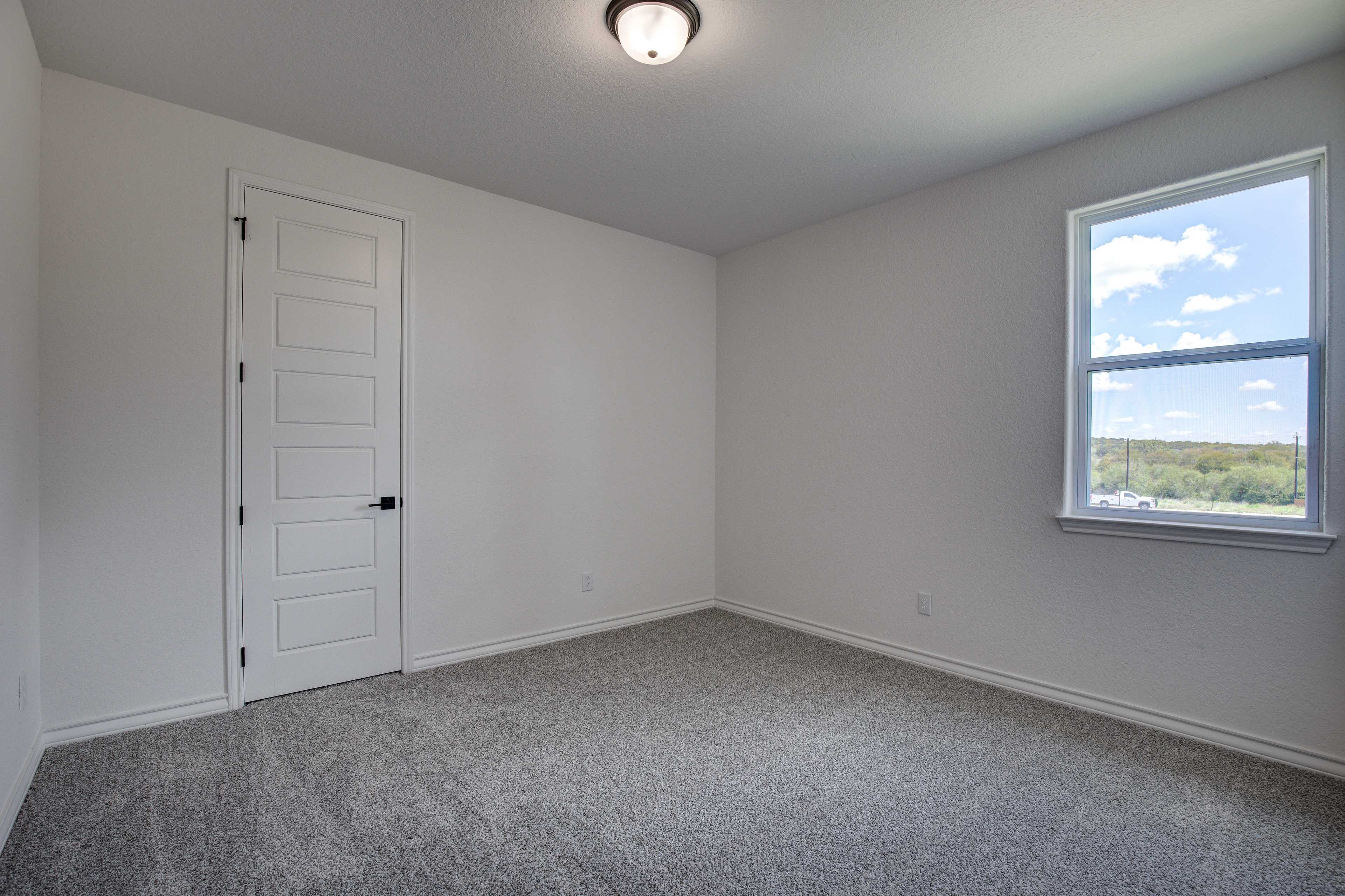 Spacious secondary bedroom in The Lanier by Davidson Homes with white walls, gray carpet, and large window overlooking landscape
