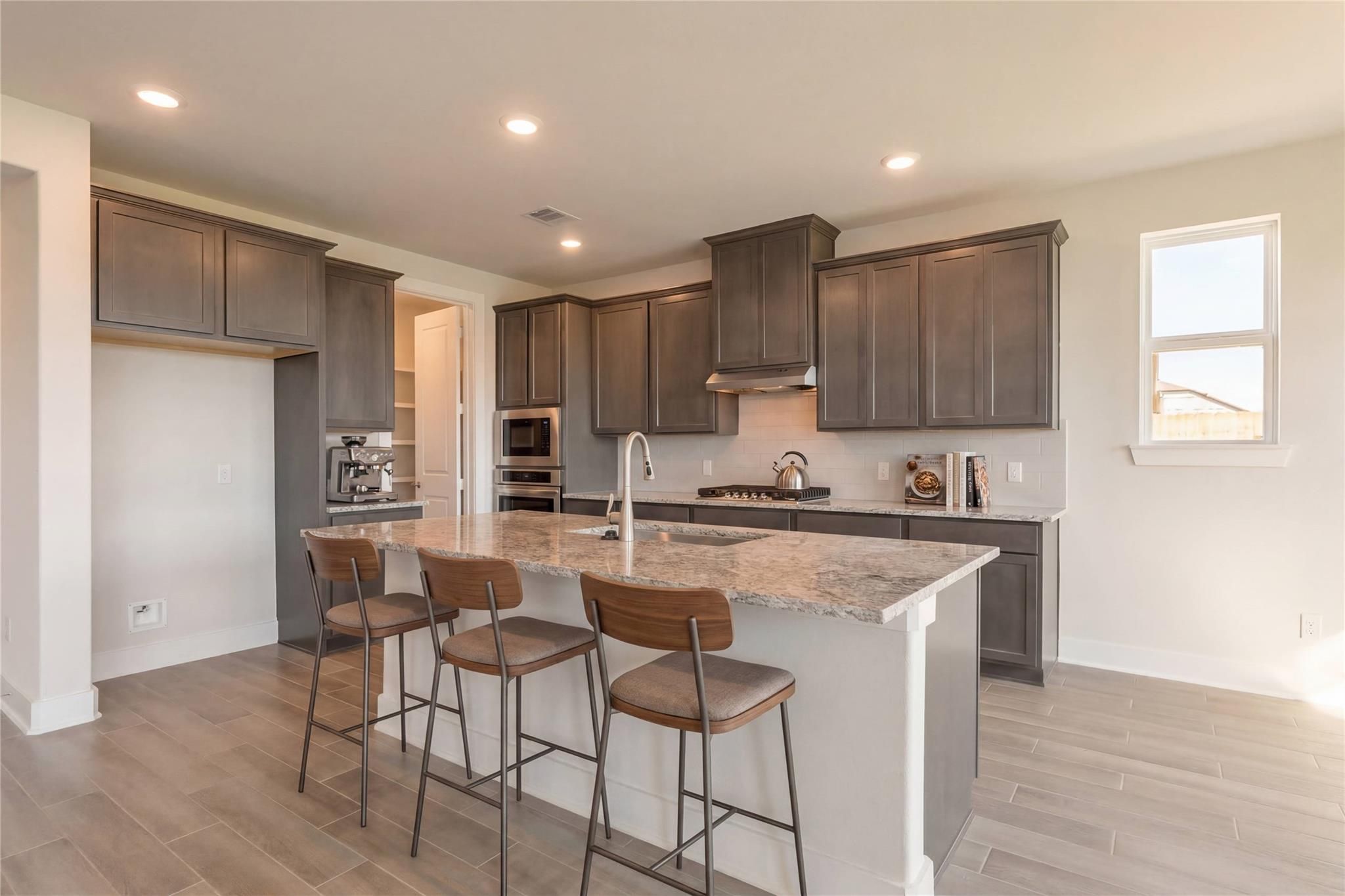 Modern gray kitchen with quartz island, stainless appliances, and bar stools in Davidson Homes The Philip A, Lago Mar, Texas City