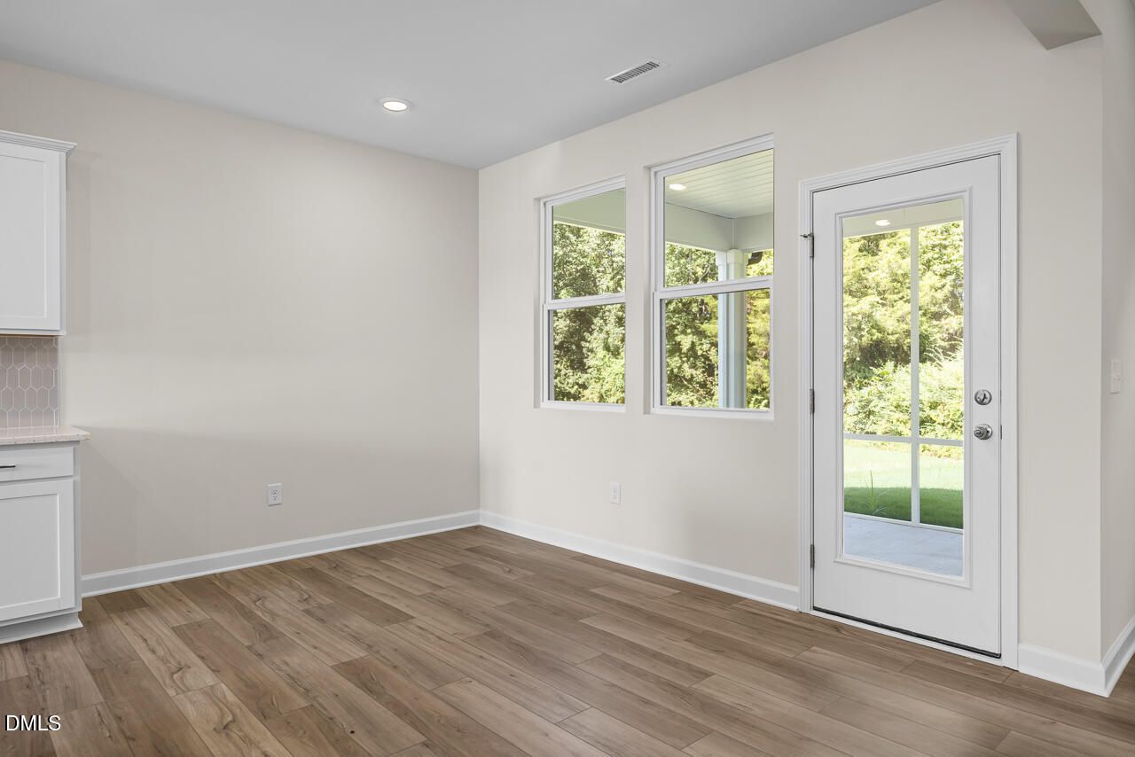Bright dining area with wood-look flooring, windows, and glass-paneled door to patio in Davidson Homes Willow C, Zebulon NC