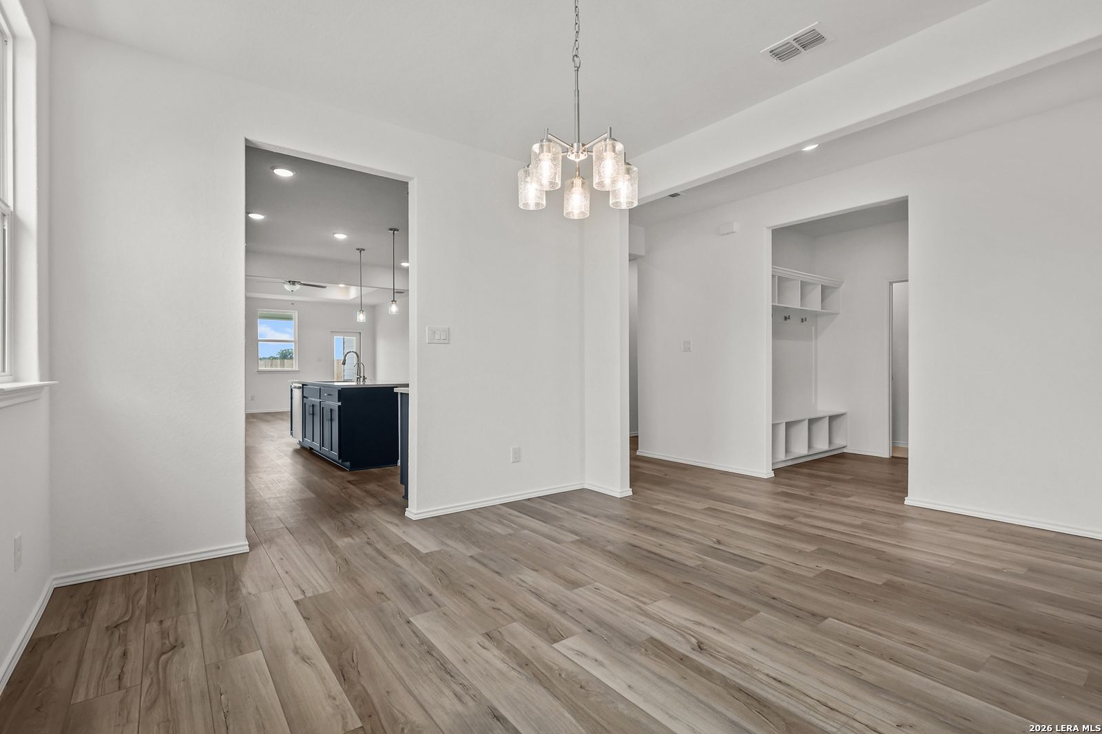 Open dining area with modern glass chandelier, navy kitchen island, luxury wood floors in Davidson Homes The Glenwood E, Elmendorf TX