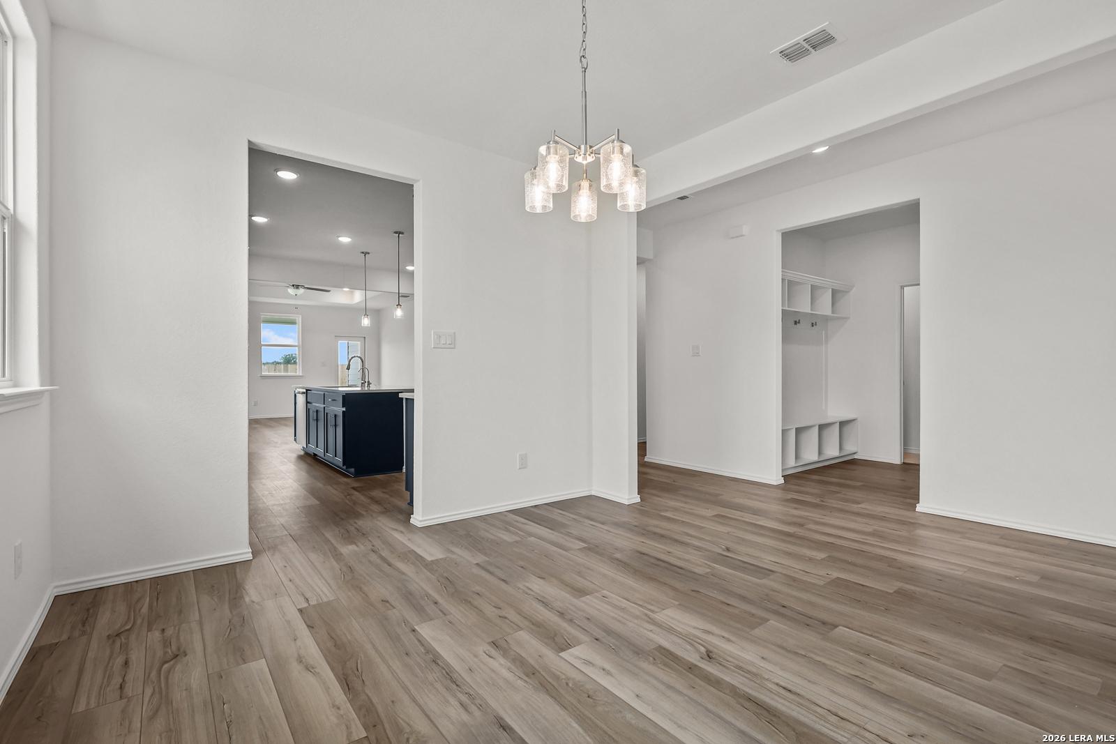Open dining area with modern glass chandelier, navy kitchen island, luxury wood floors in Davidson Homes The Glenwood E, Elmendorf TX