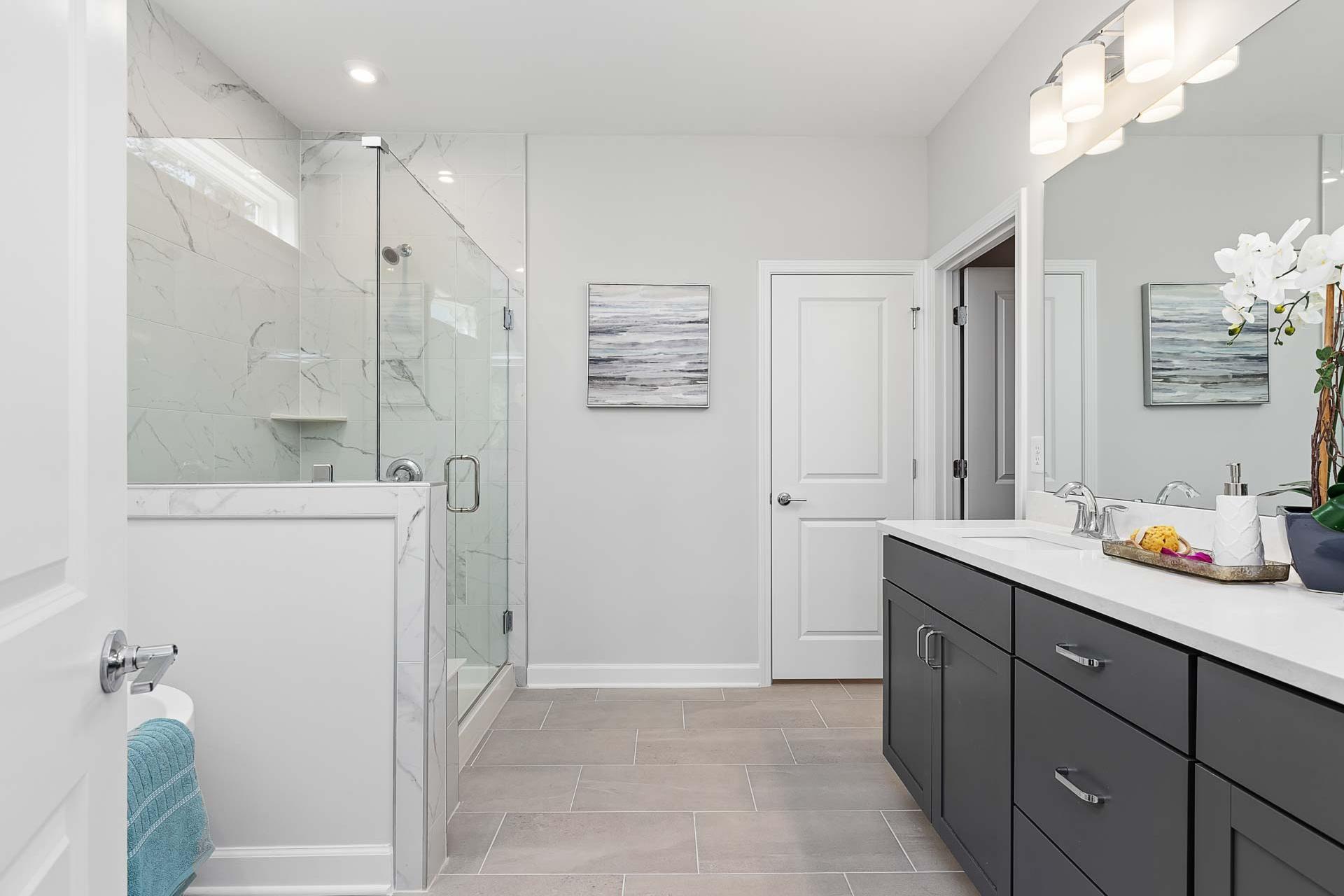 Spacious modern bathroom at Glenmere in Knightdale NC with frameless glass shower, marble vanity, and dark cabinets